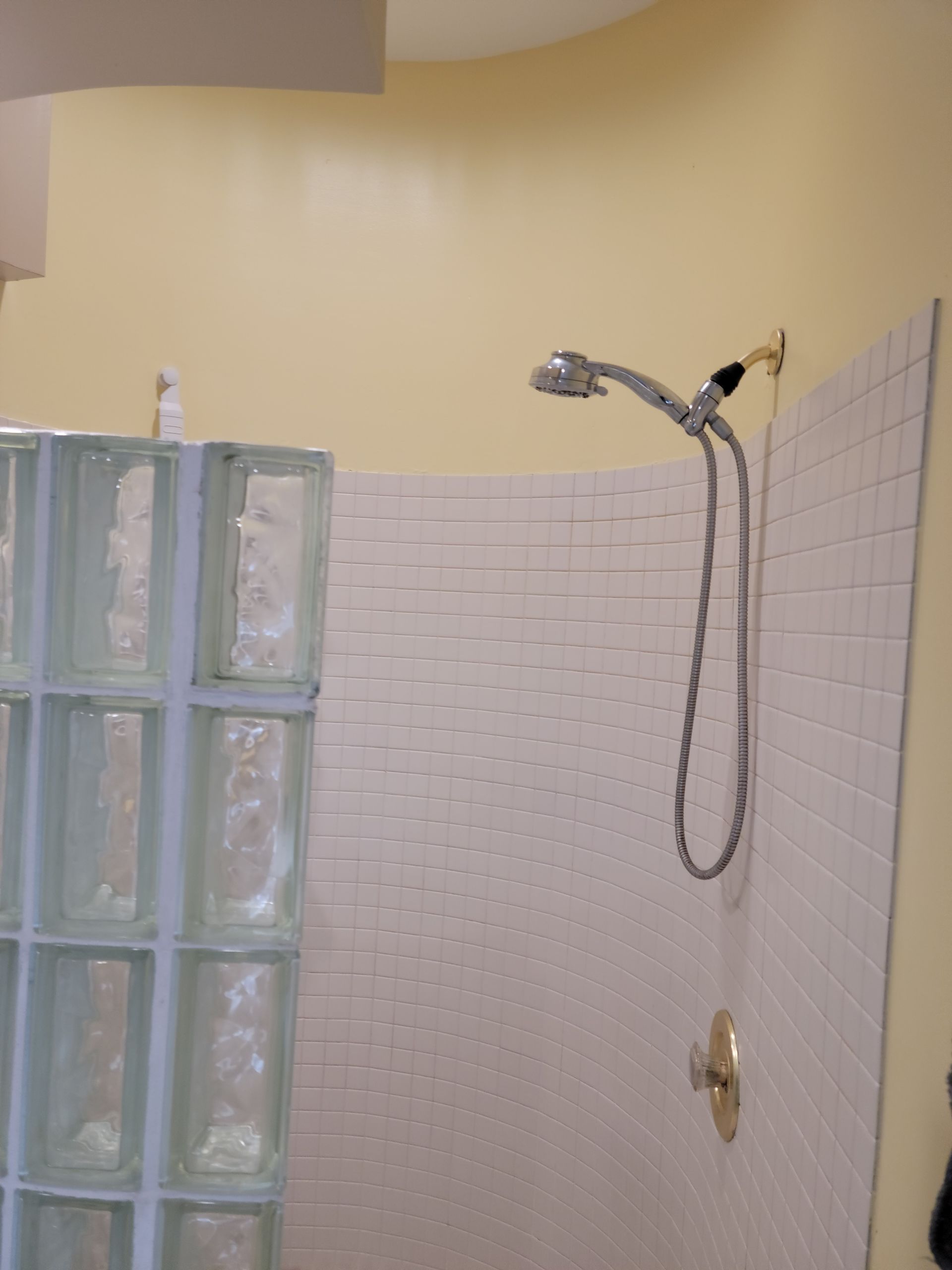Bathroom shower with white tile, glass block wall, and handheld showerhead on cream walls