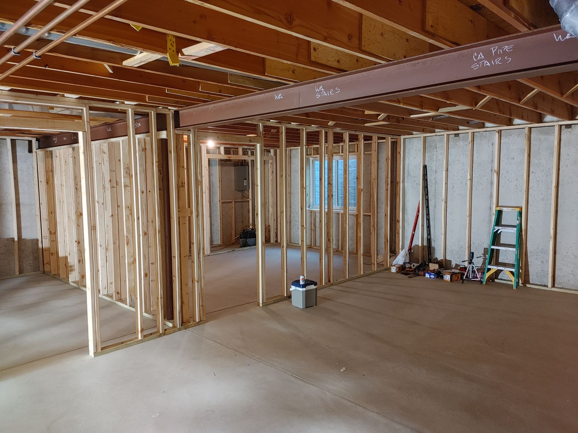 Unfinished basement framing with exposed studs, concrete floor, and construction tools along the wall.