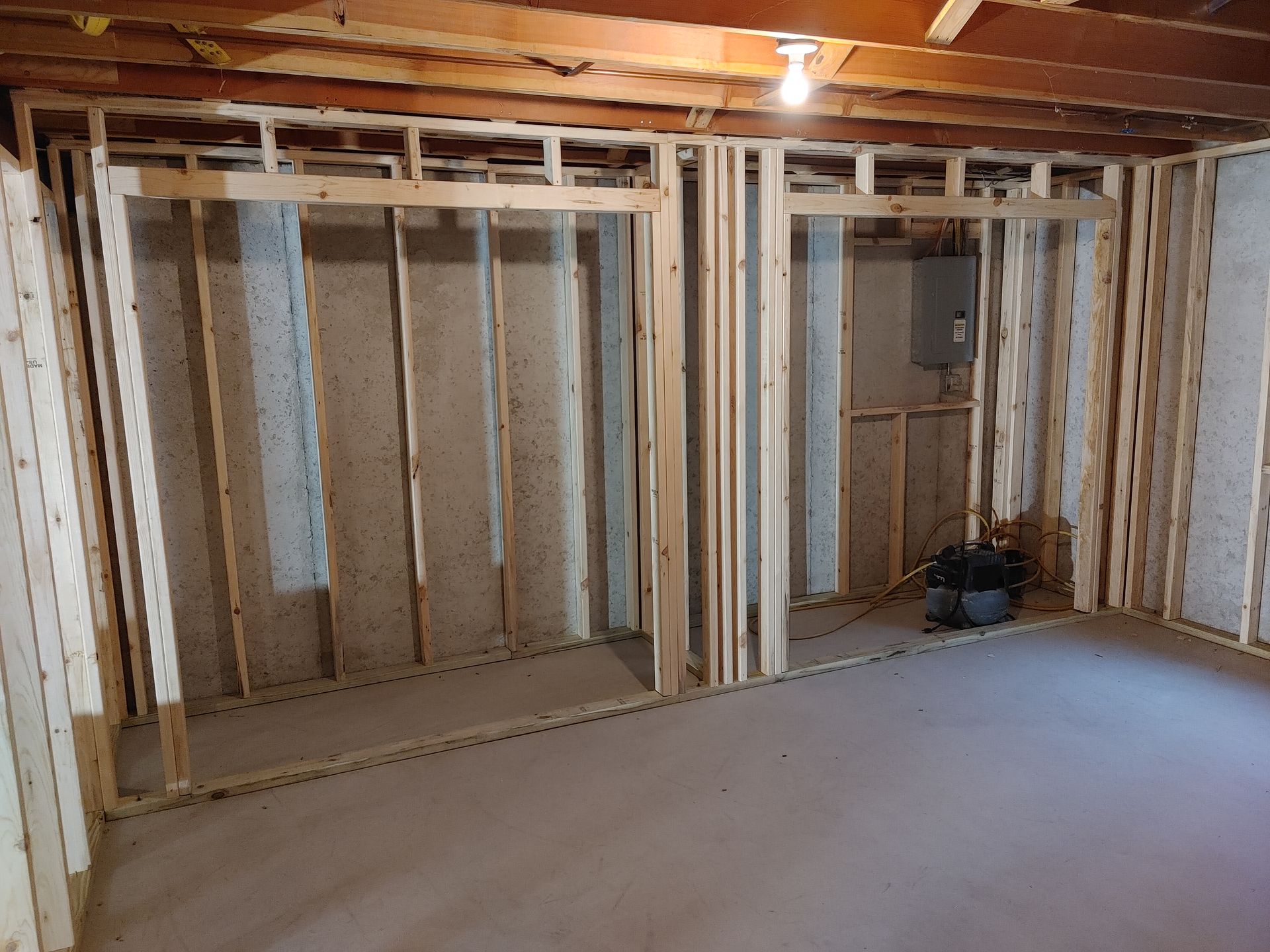 Unfinished basement with exposed studs, insulated walls, and a bare concrete floor under ceiling lights