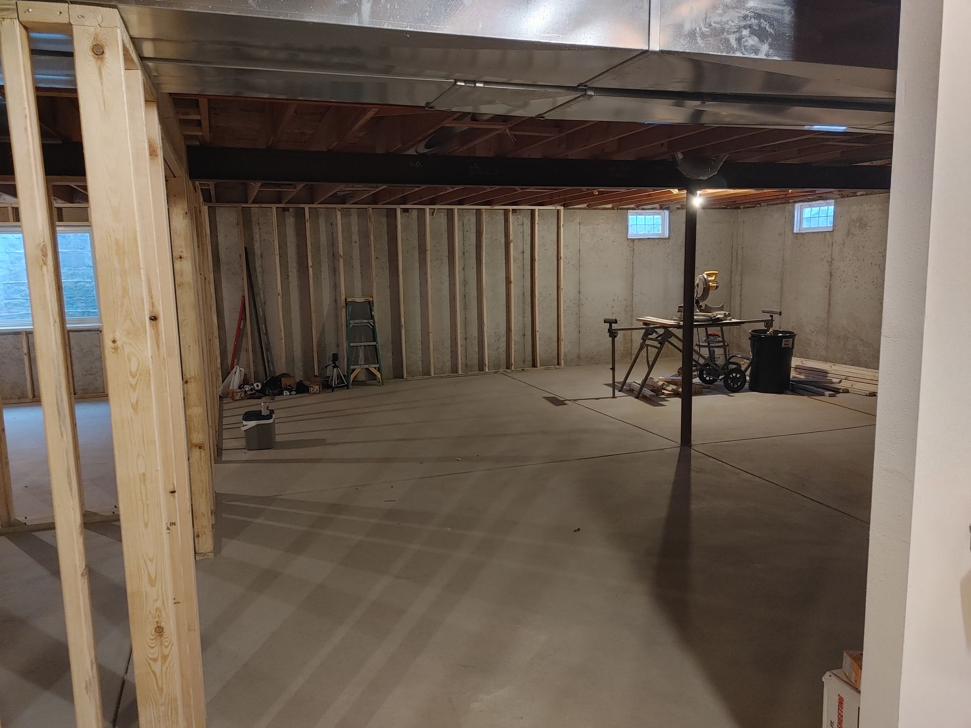 Unfinished basement with exposed beams, concrete floor, and scattered tools and equipment.