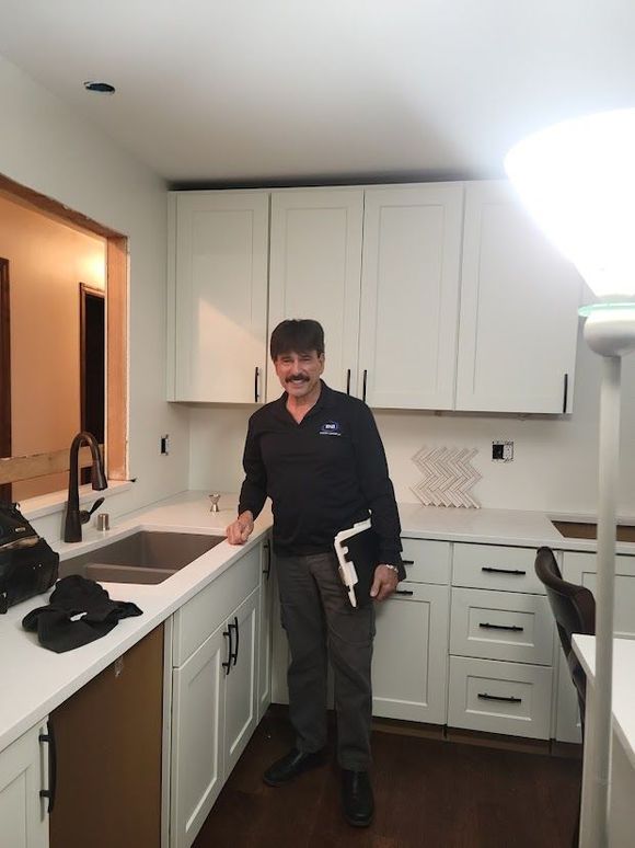 Man standing in a bright white kitchen beside the sink and counter, holding a book.