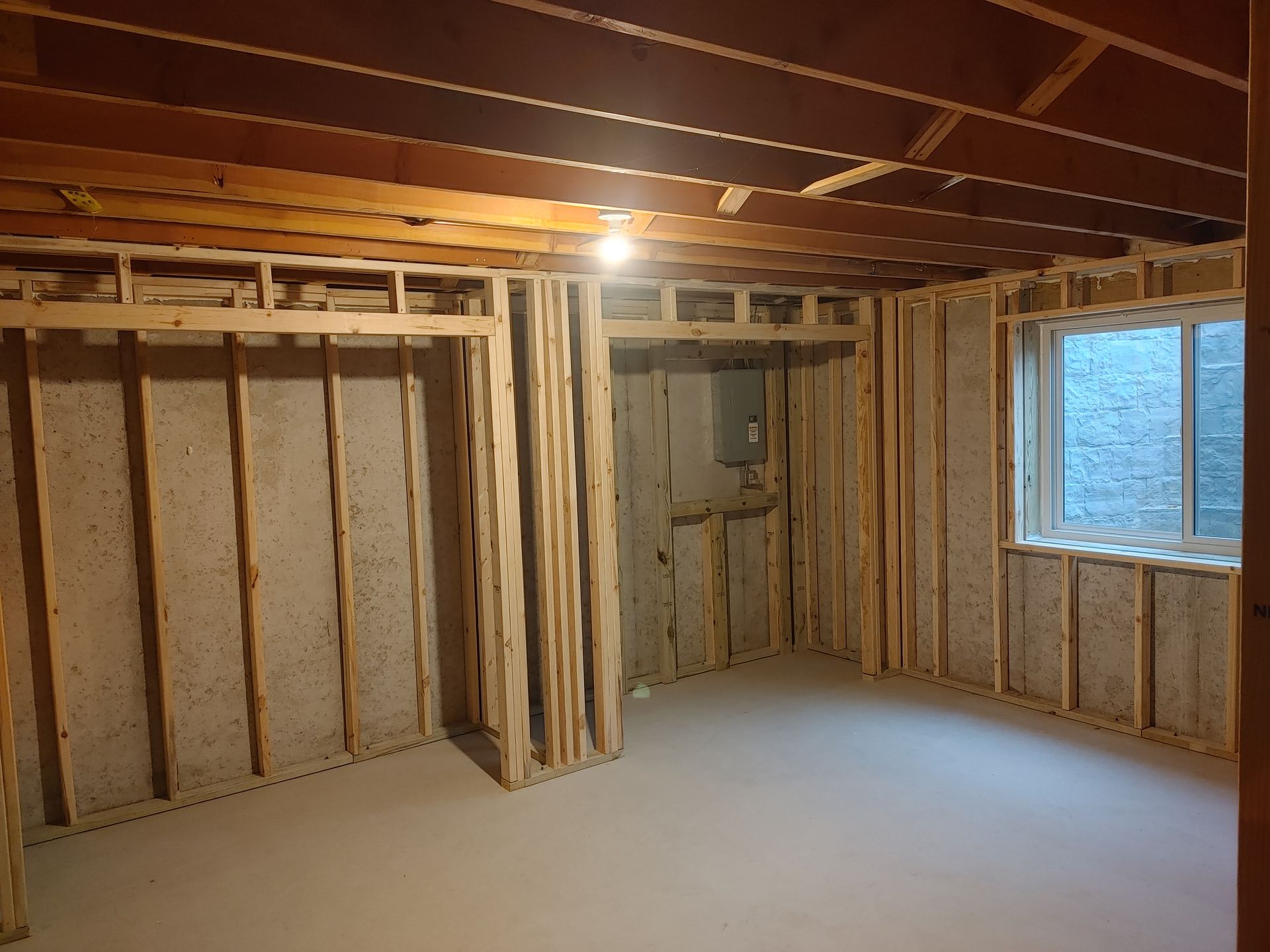 Unfinished basement room with exposed studs, insulation, wood beams, and a window.