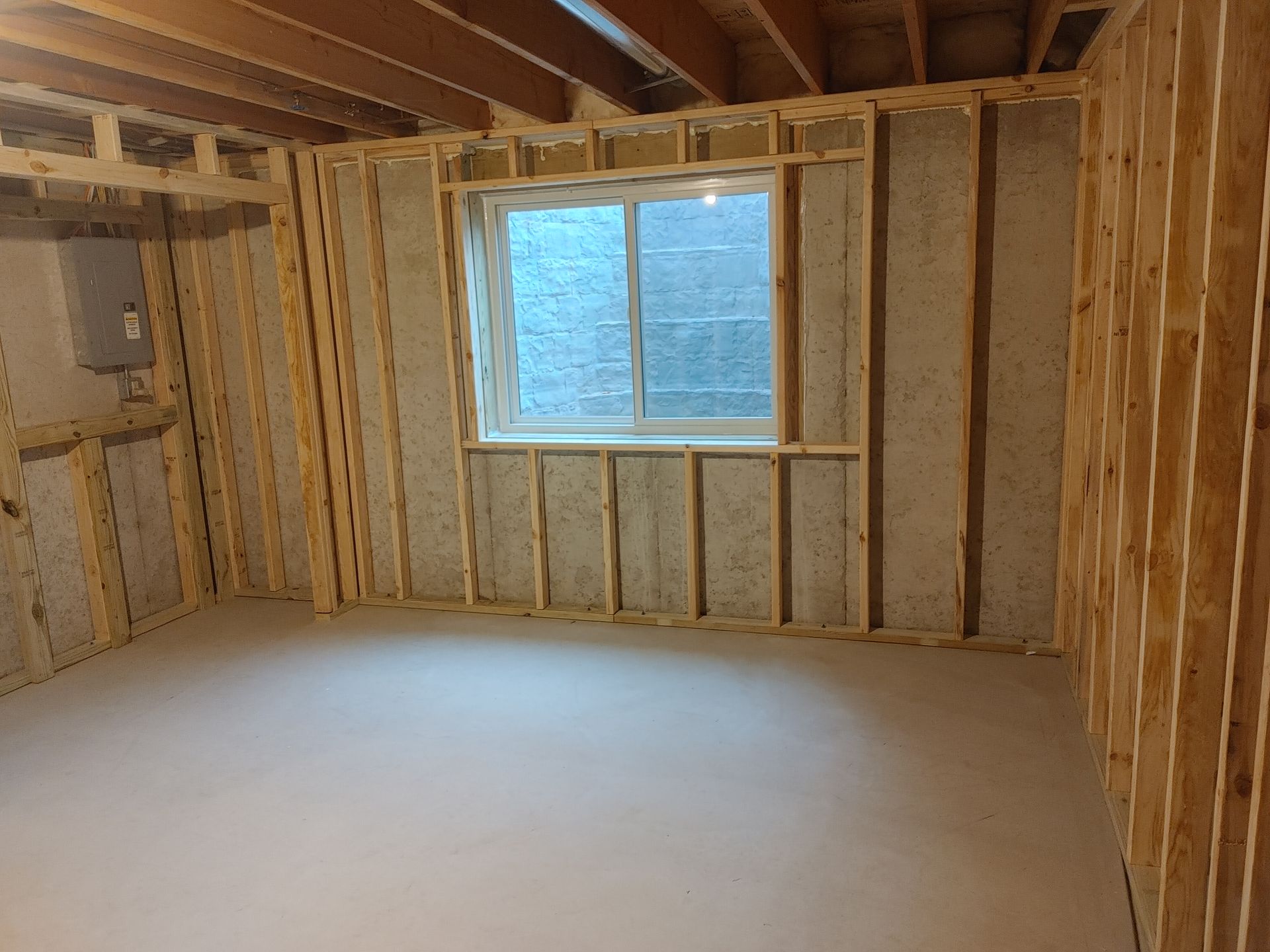 Unfinished basement room with exposed insulation, bare studs, and a small window.