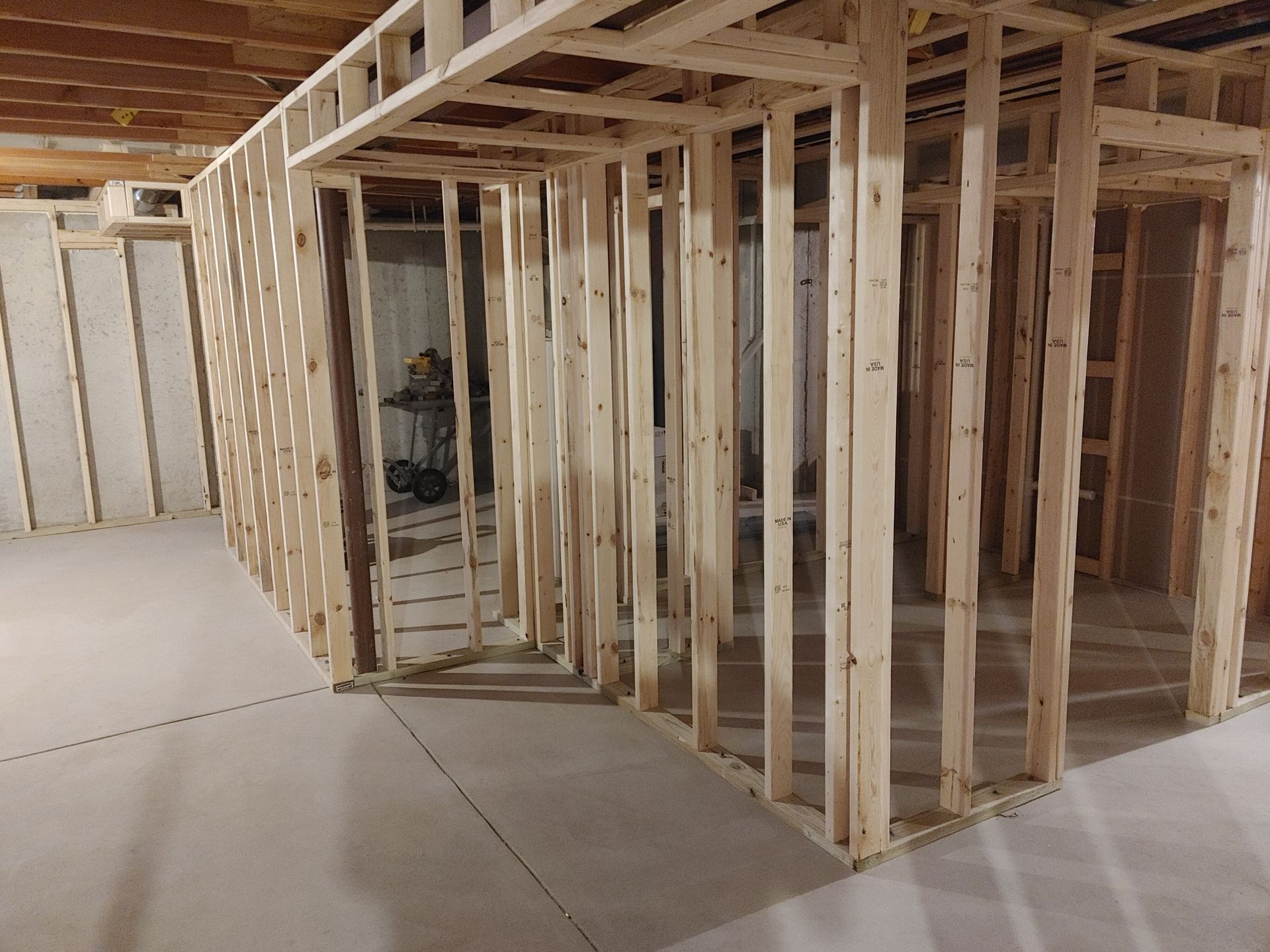 Framed basement interior with unfinished wood walls, ceiling joists, and concrete floor under construction