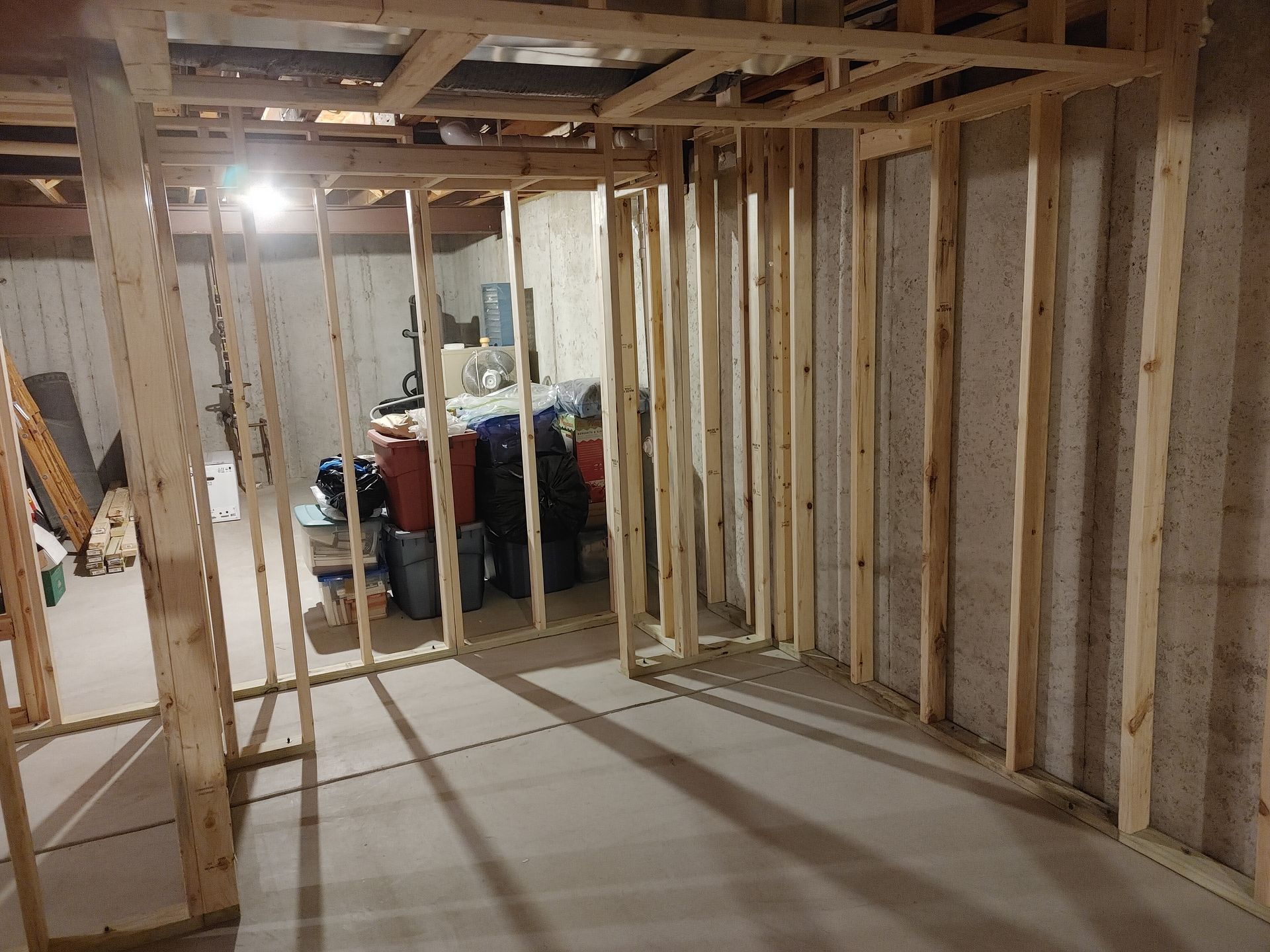 Unfinished basement with exposed wooden framing and concrete floor, storage items in the back.