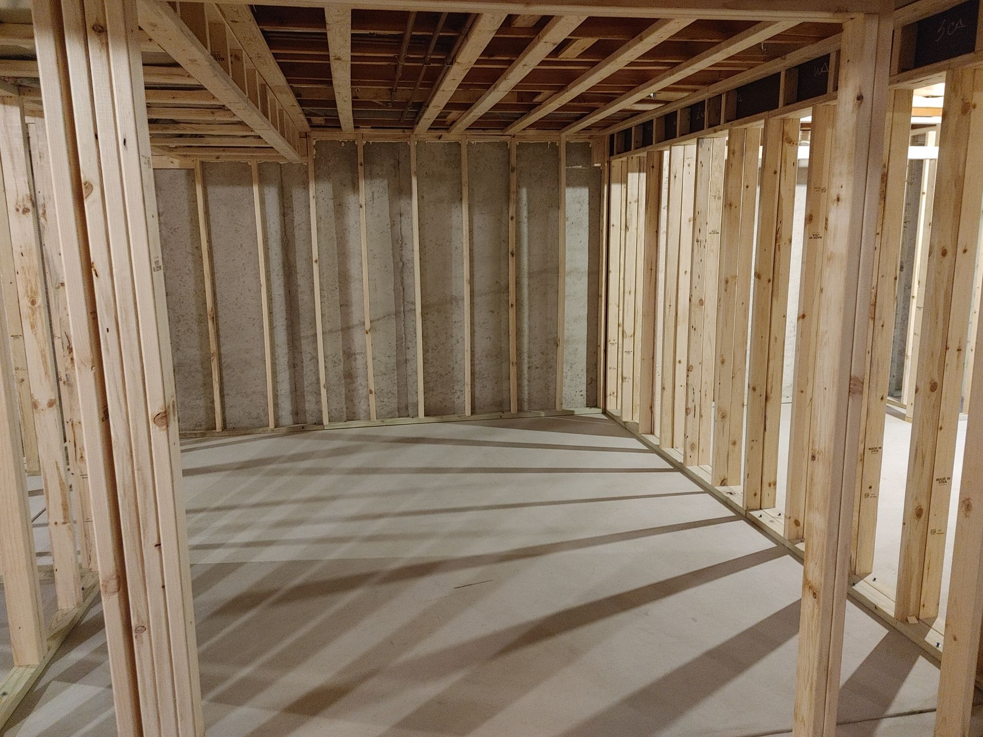 Unfinished room with exposed wooden framing, concrete floor, and open ceiling joists.