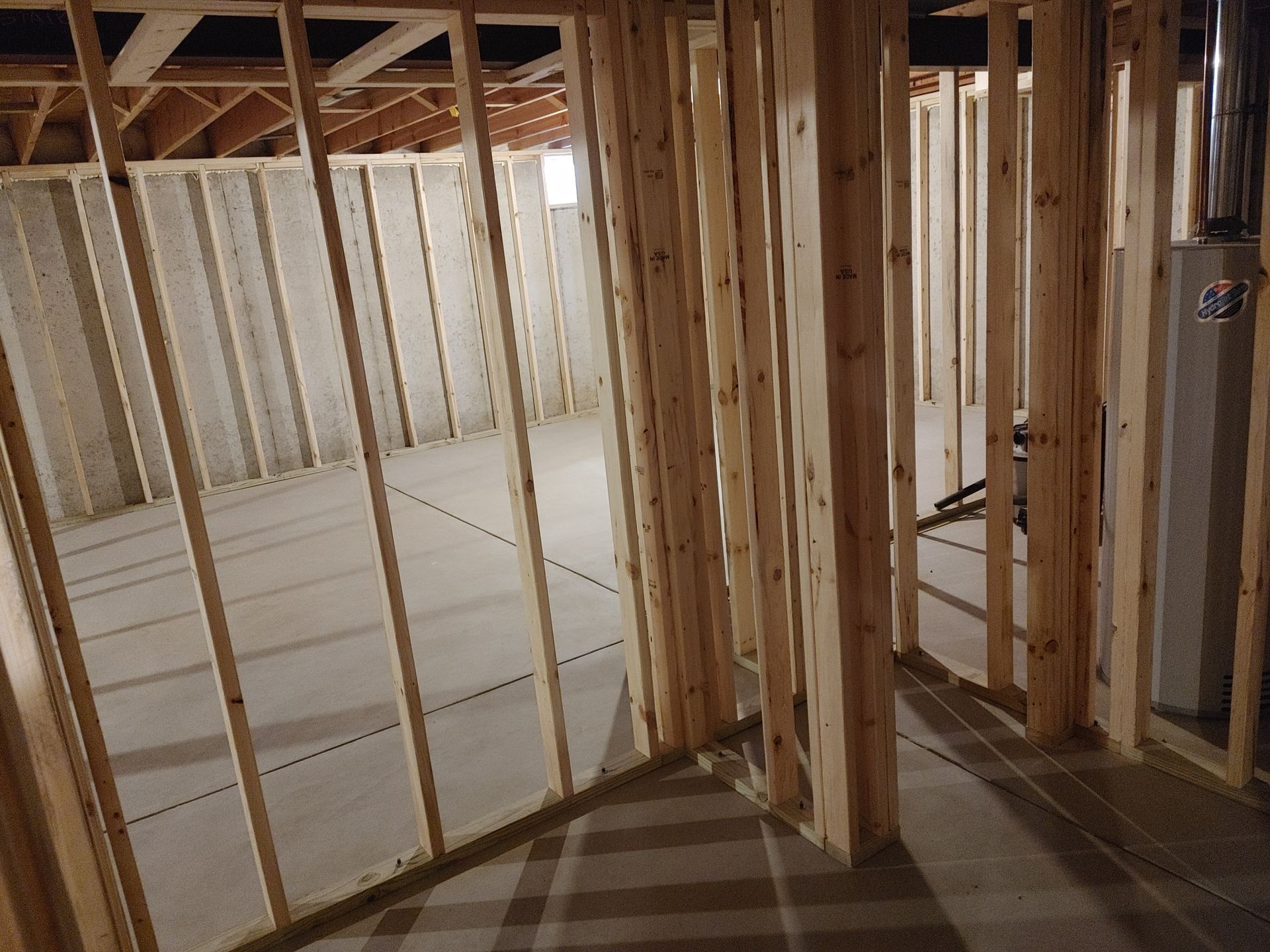 Unfinished basement framing with exposed wooden studs and concrete floor during construction