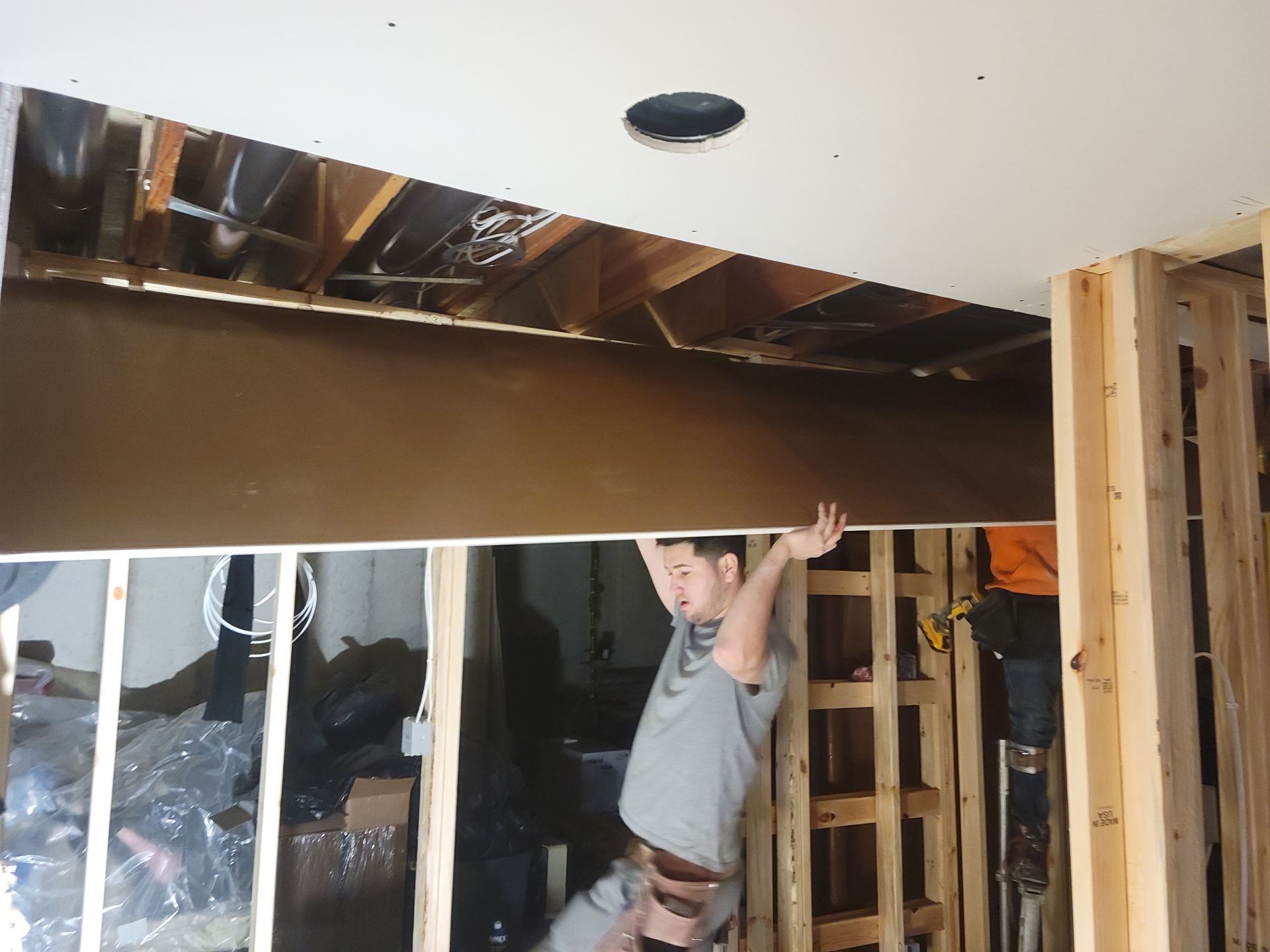 Man in a basement under construction holding up a beam beneath an unfinished ceiling