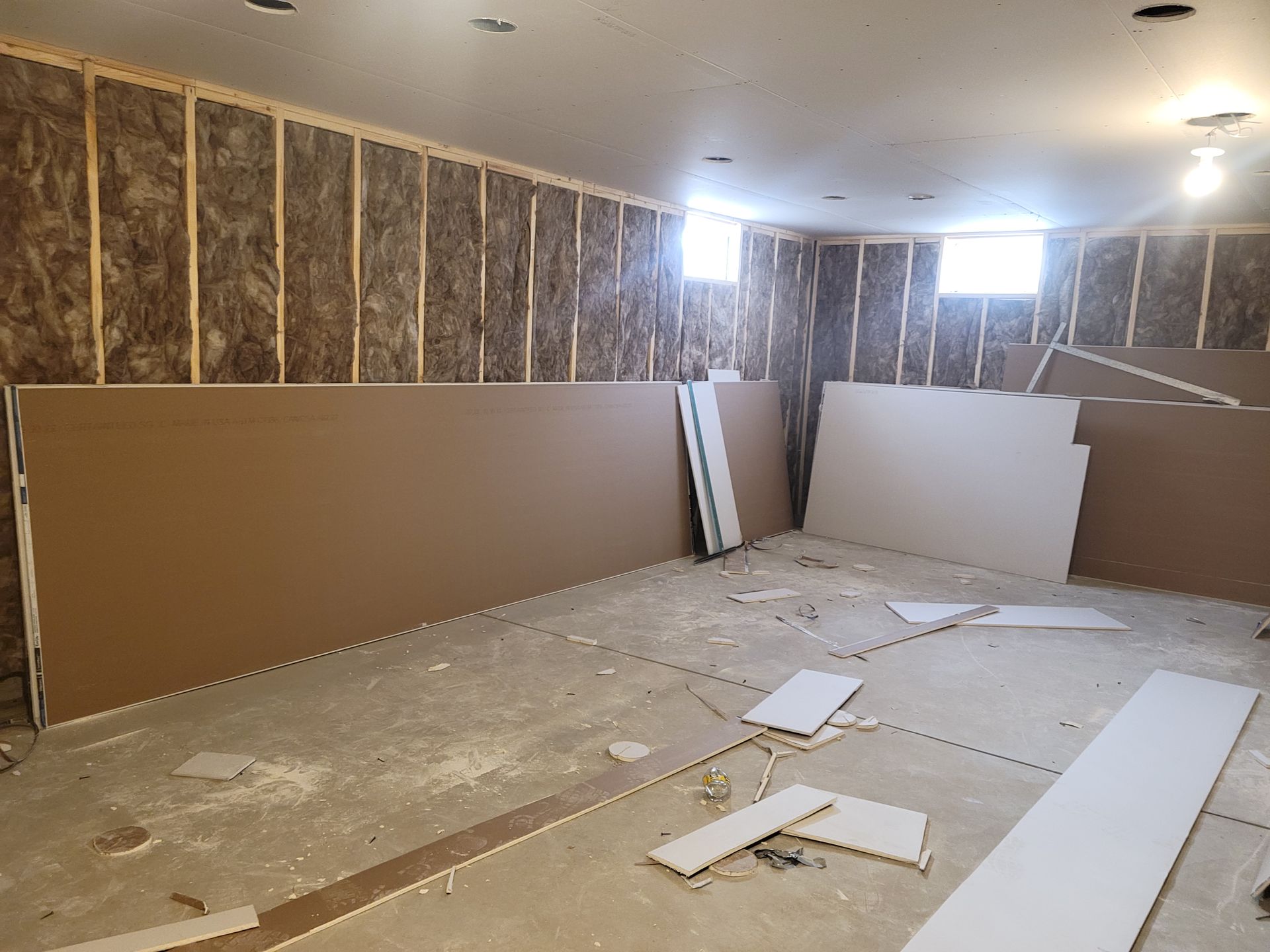 Partially finished room with drywall panels, insulation, and debris on the floor