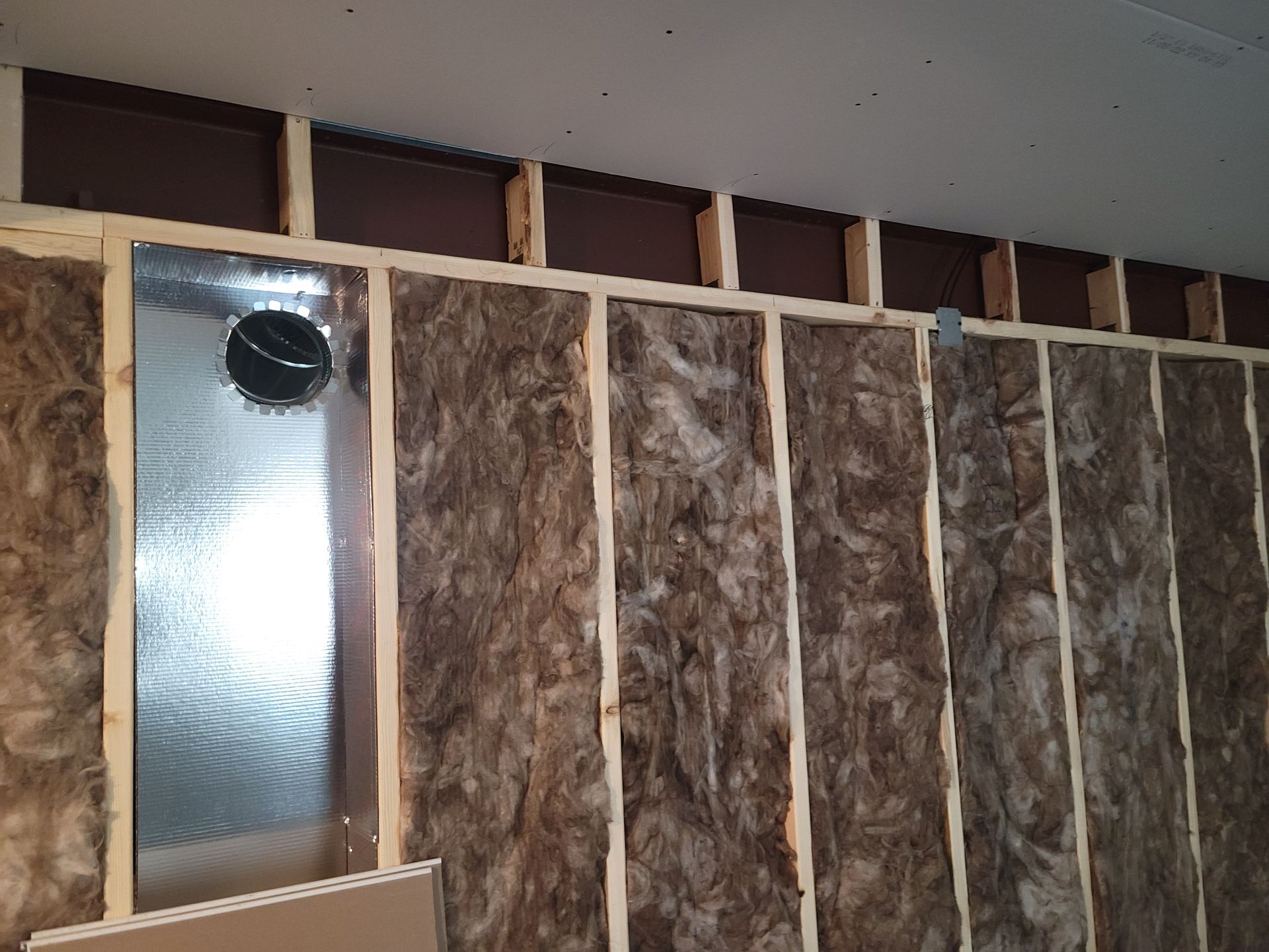 Insulated wall under construction with exposed studs and a small window opening