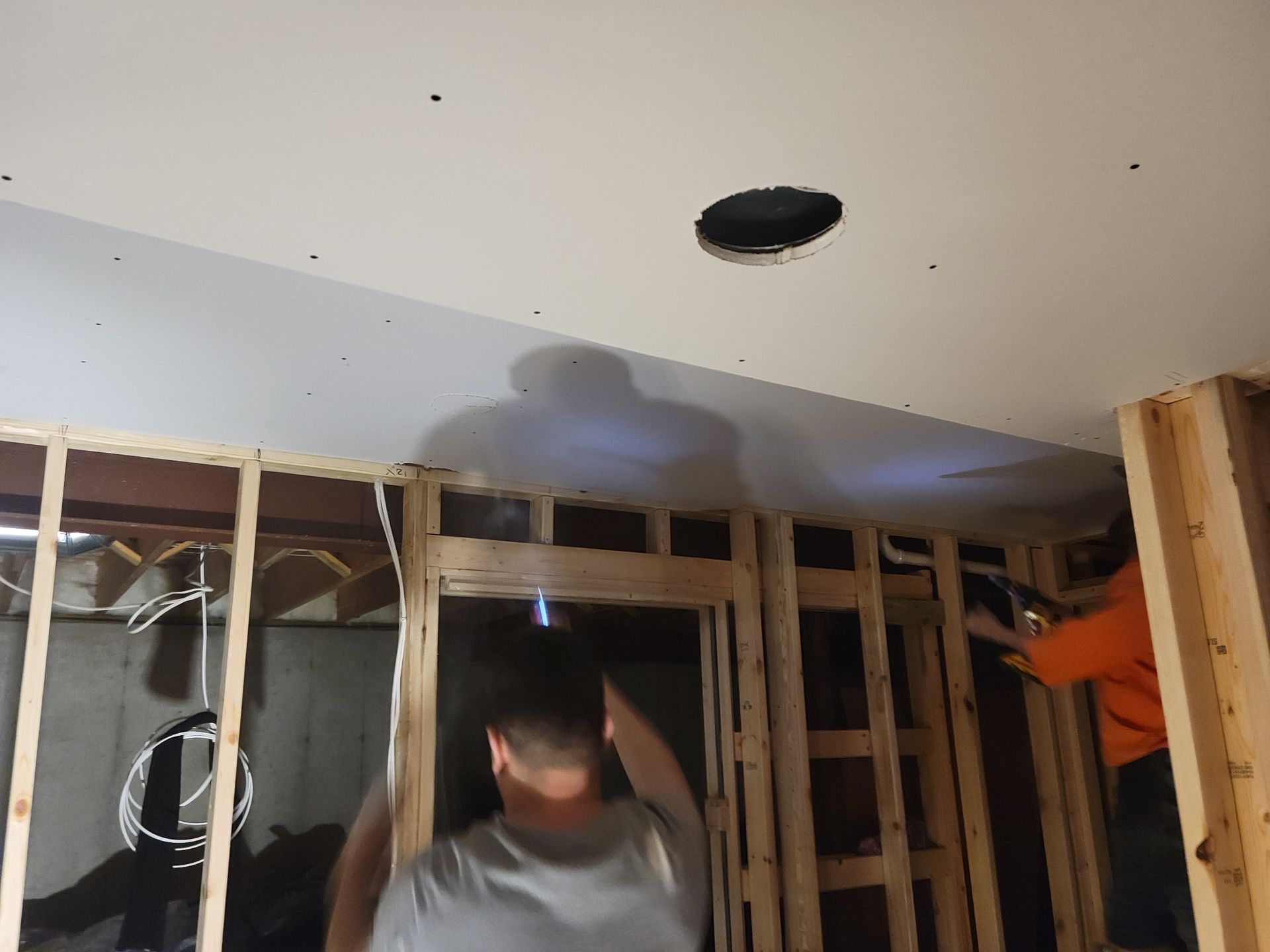 Man installing ceiling drywall around a recessed light opening in a framed room