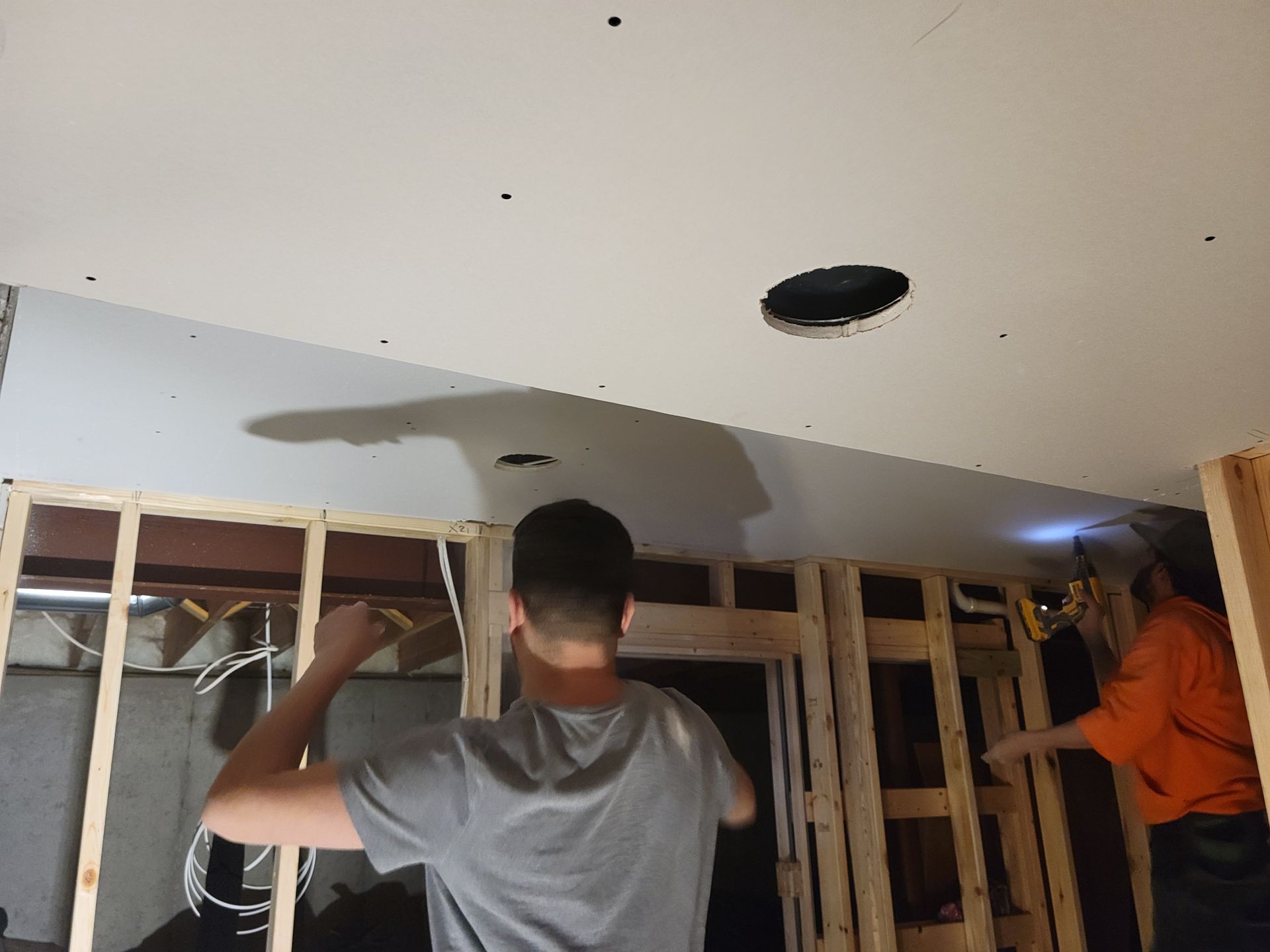 People working on exposed wall framing and ceiling in a room under renovation