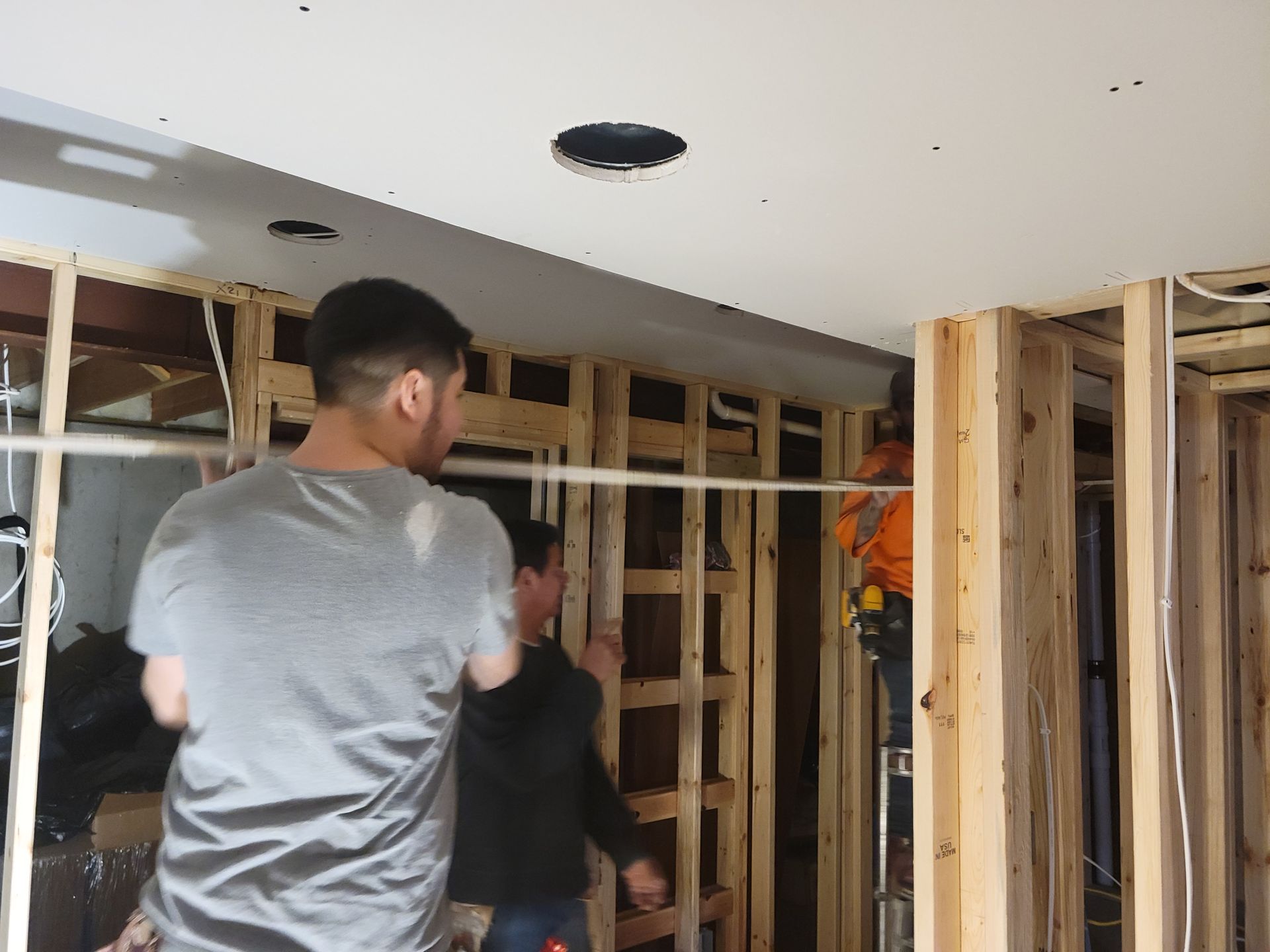 Two workers framing a room with exposed studs and drywall under renovation