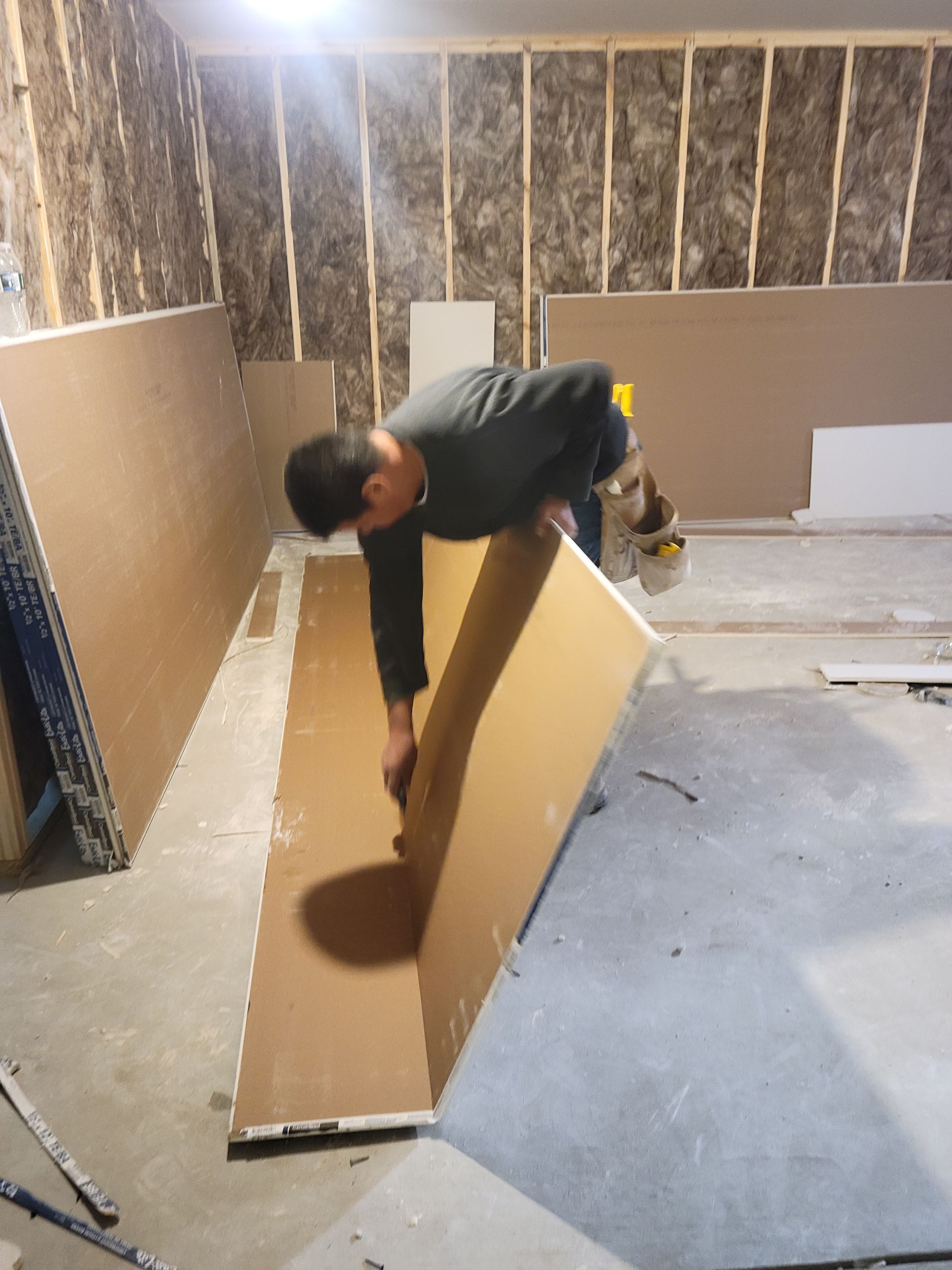 Person folding a large cardboard panel in an unfinished room with exposed insulation and concrete floor