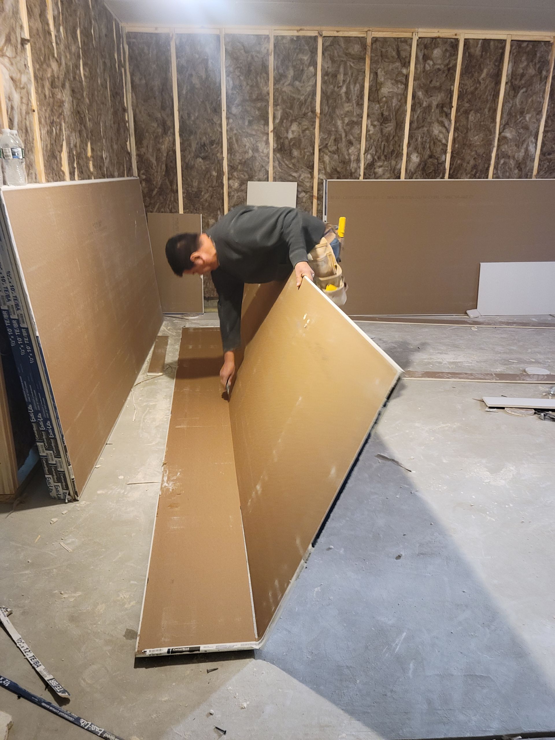 Person lifting drywall panel in an unfinished room under construction