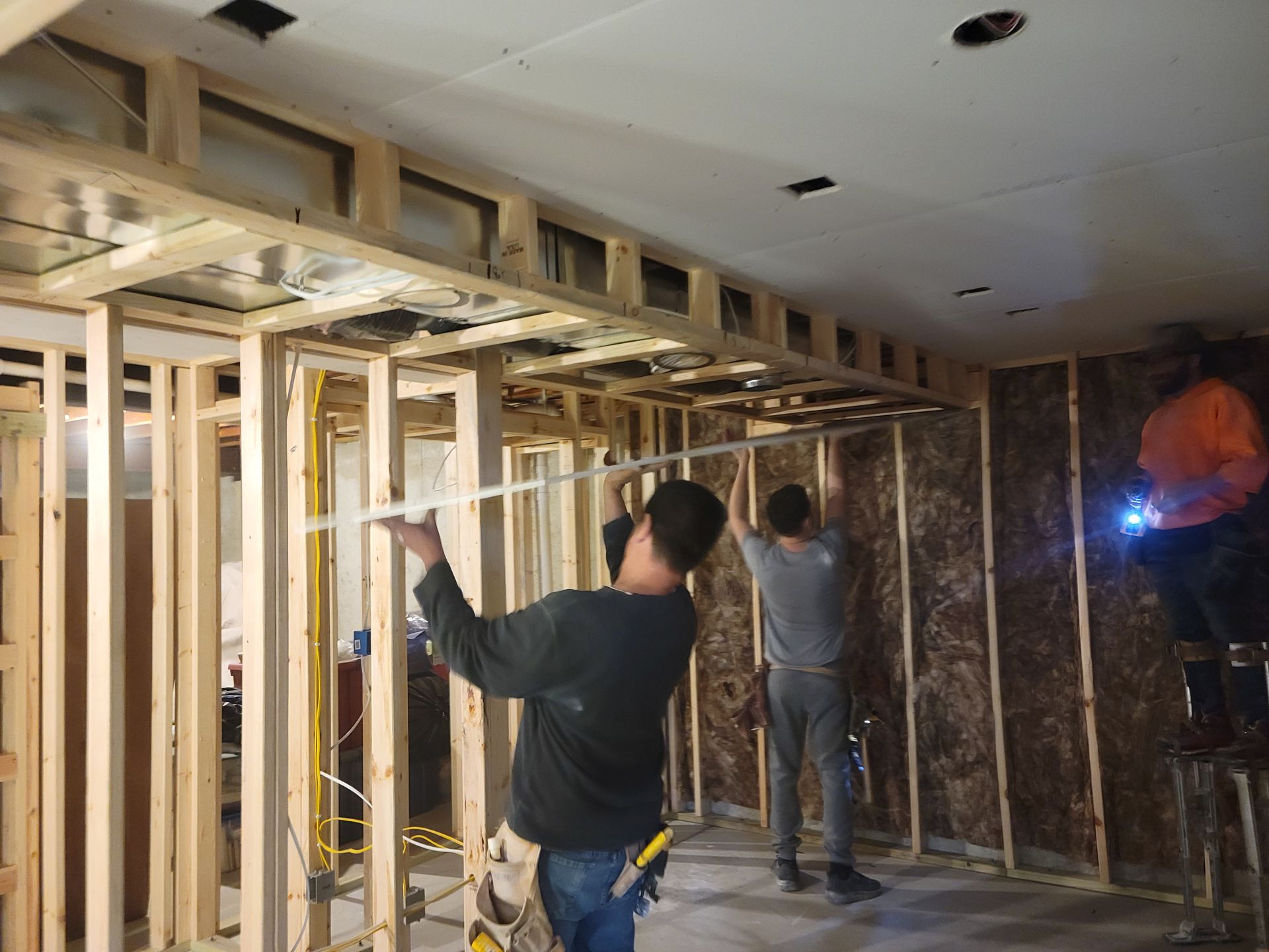 Workers framing interior walls in an unfinished room during renovation.