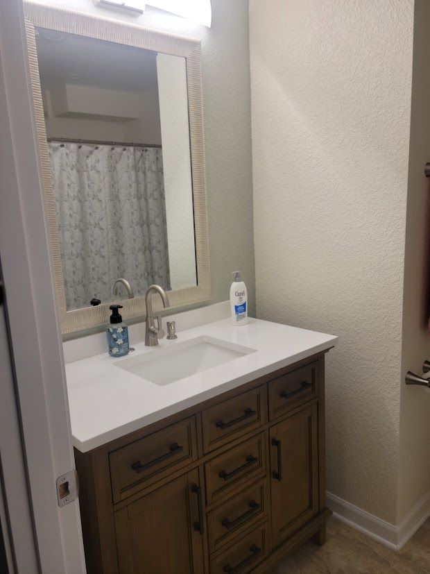Bathroom vanity with sink, large mirror, and soap dispenser beside a shower curtain.