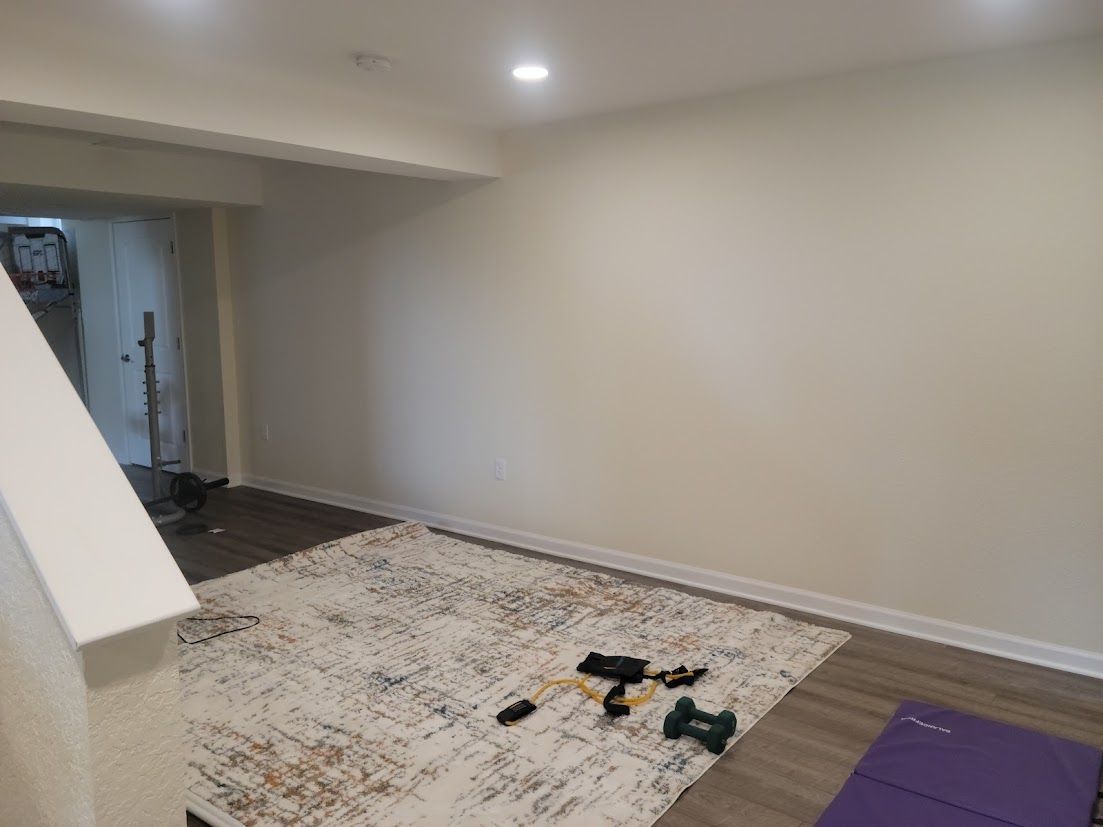 Empty basement room with beige walls, recessed lights, unfinished floor, rug, and scattered tools.