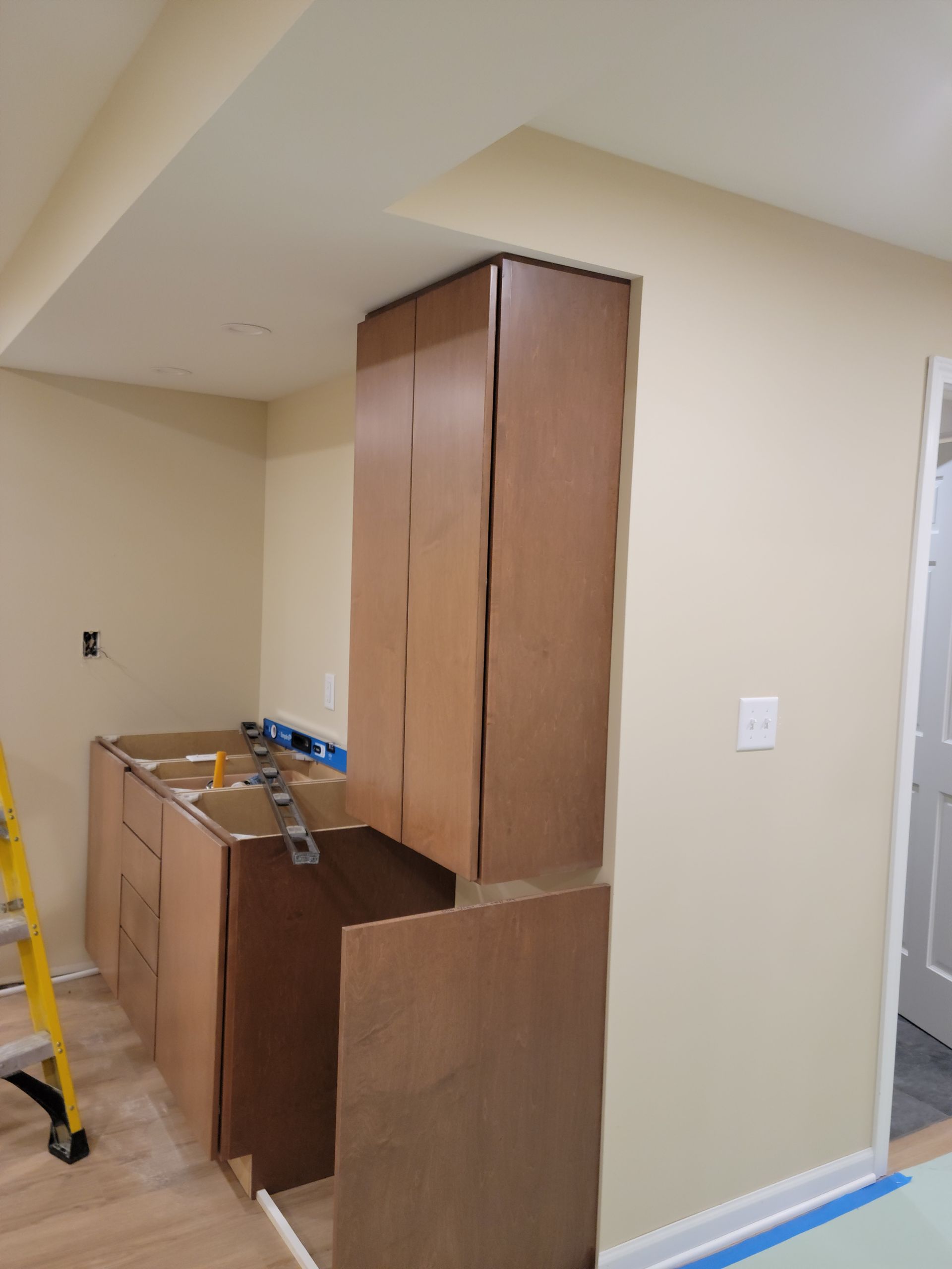 Partially assembled wooden cabinet in a beige room with a ladder and countertop nearby