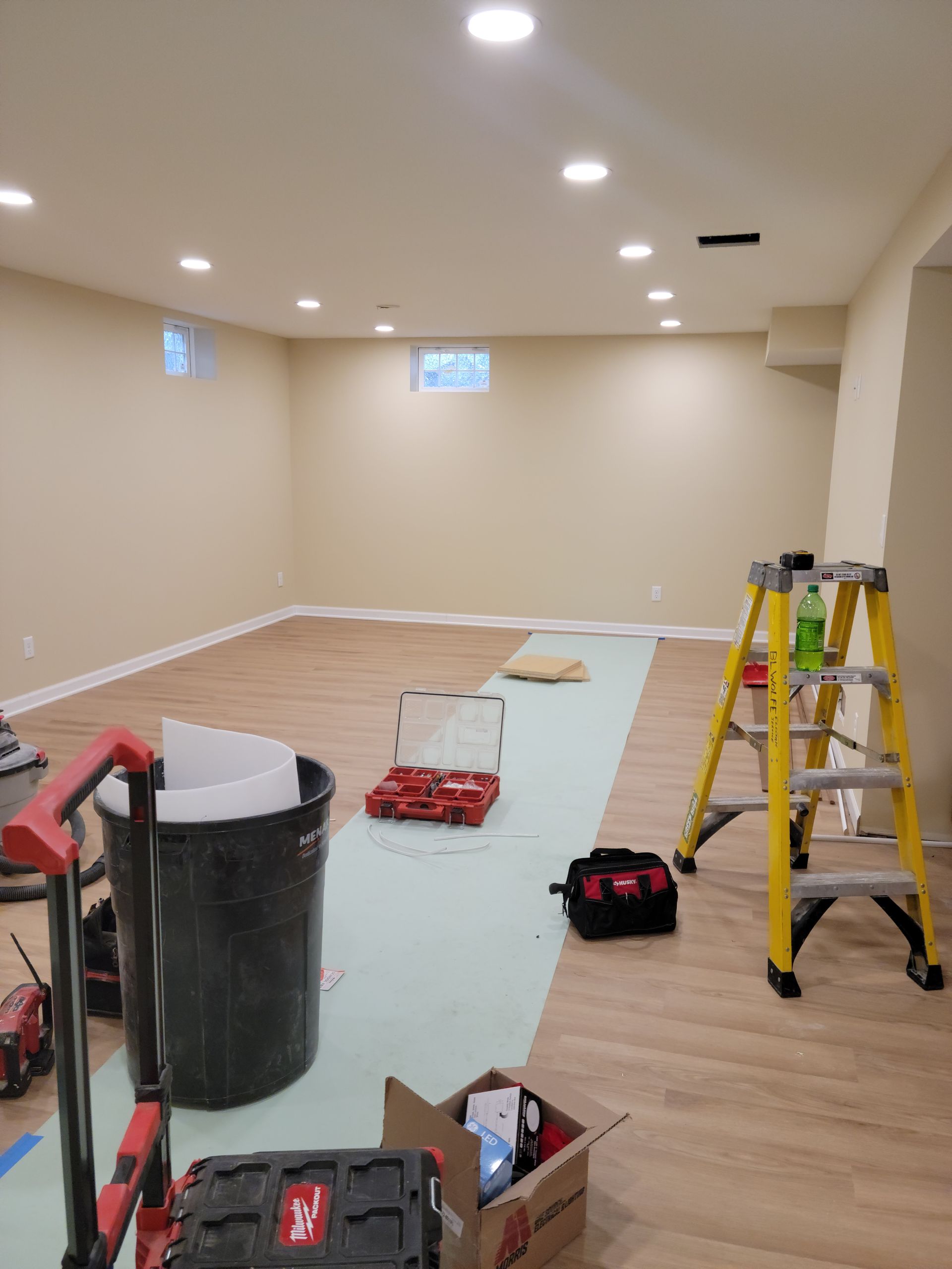 Partially renovated room with tools, ladders, and protective floor covering under recessed lights