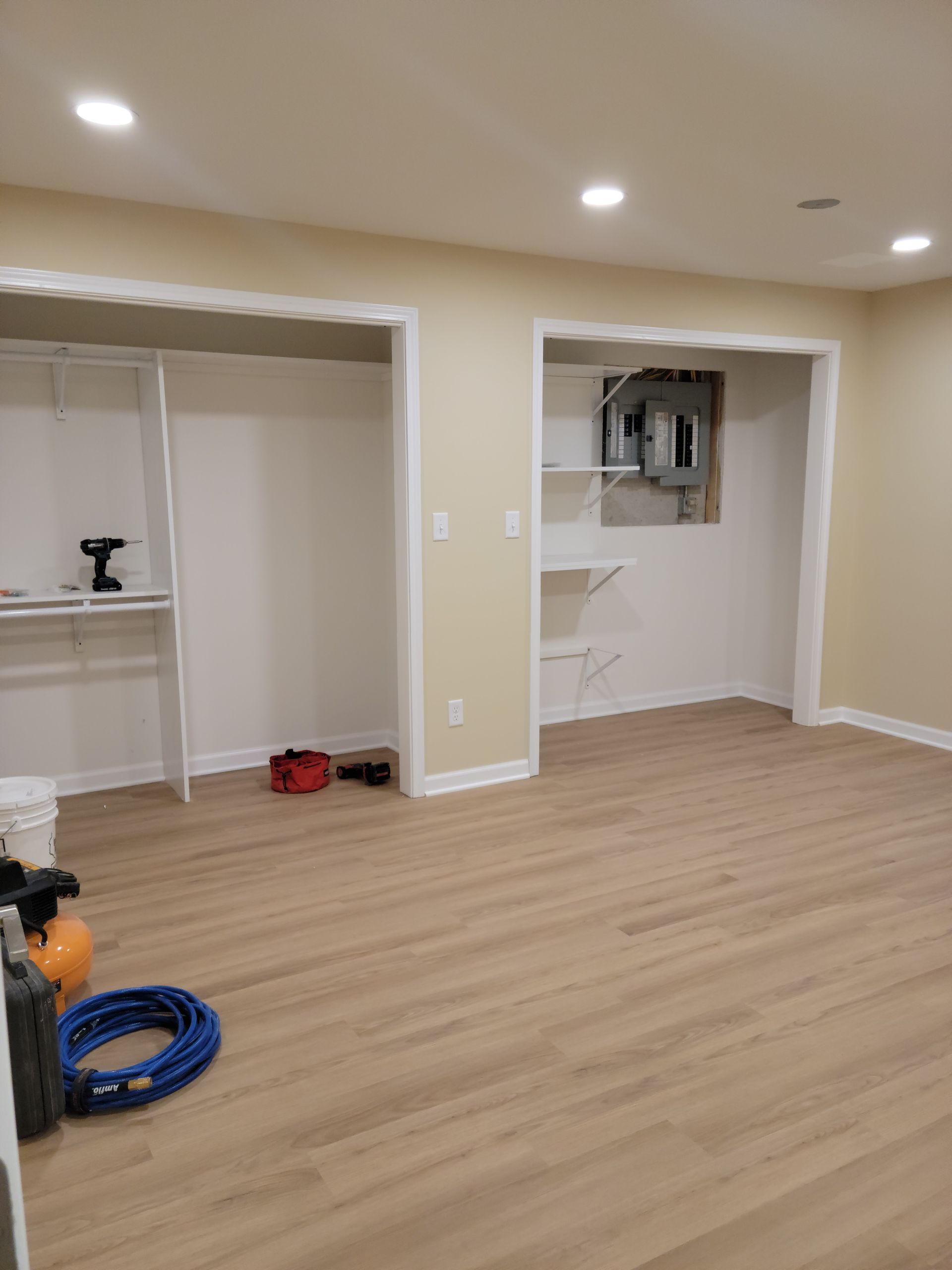 Empty beige room with light wood floor, recessed lights, and open closets/cabinets.