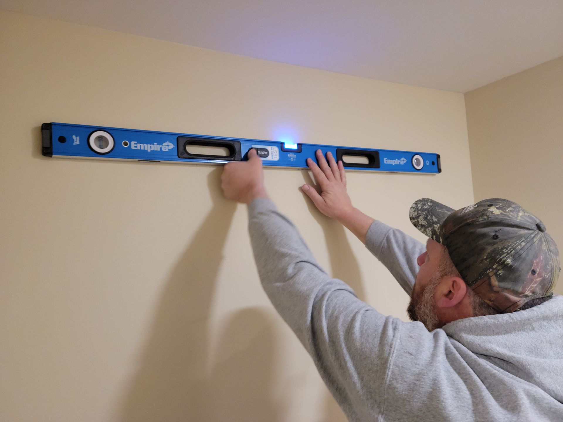 Man using a blue level to hang a wall shelf on a beige wall.