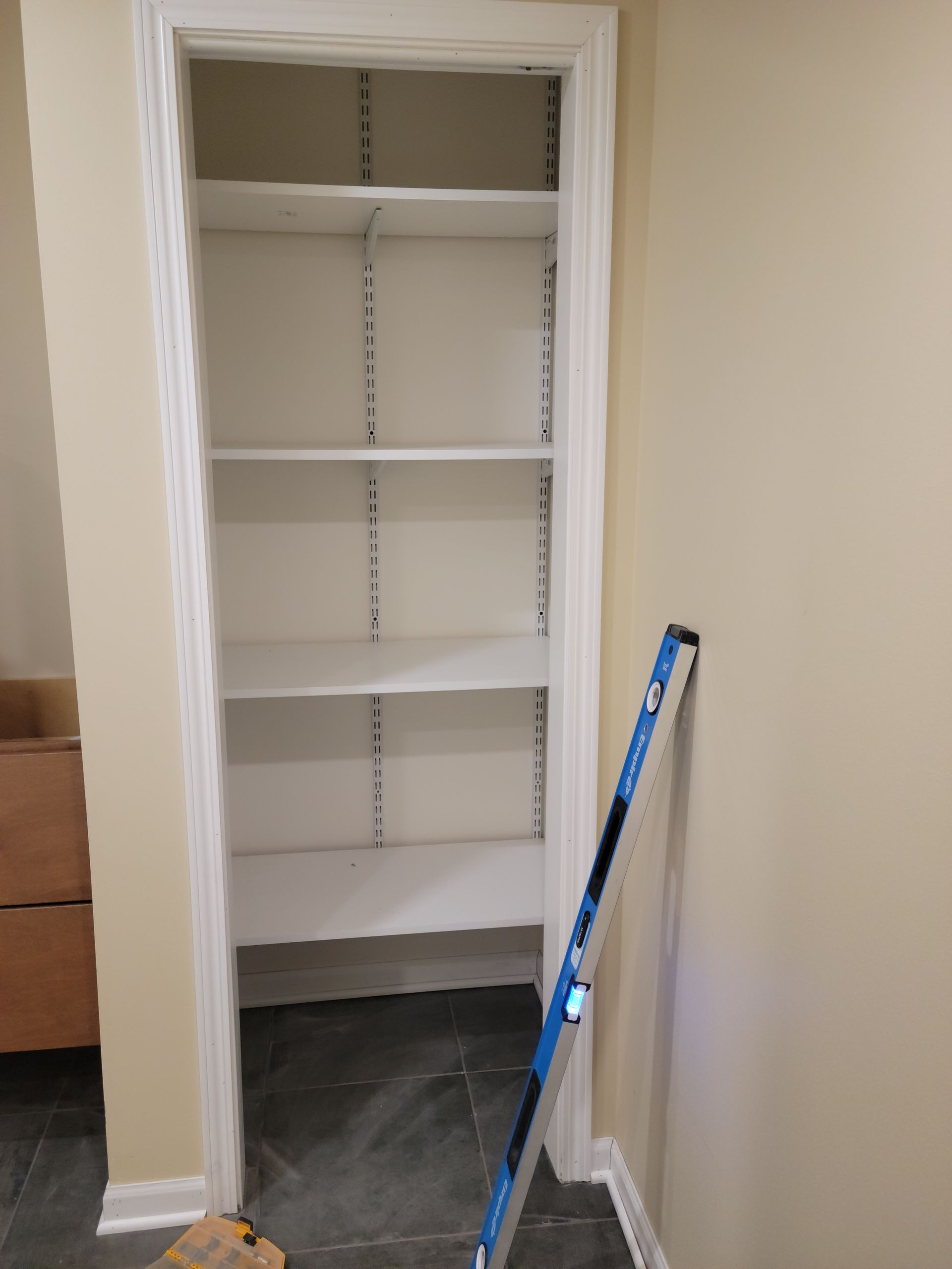 Empty closet with white shelves and a blue measuring tool leaning inside.