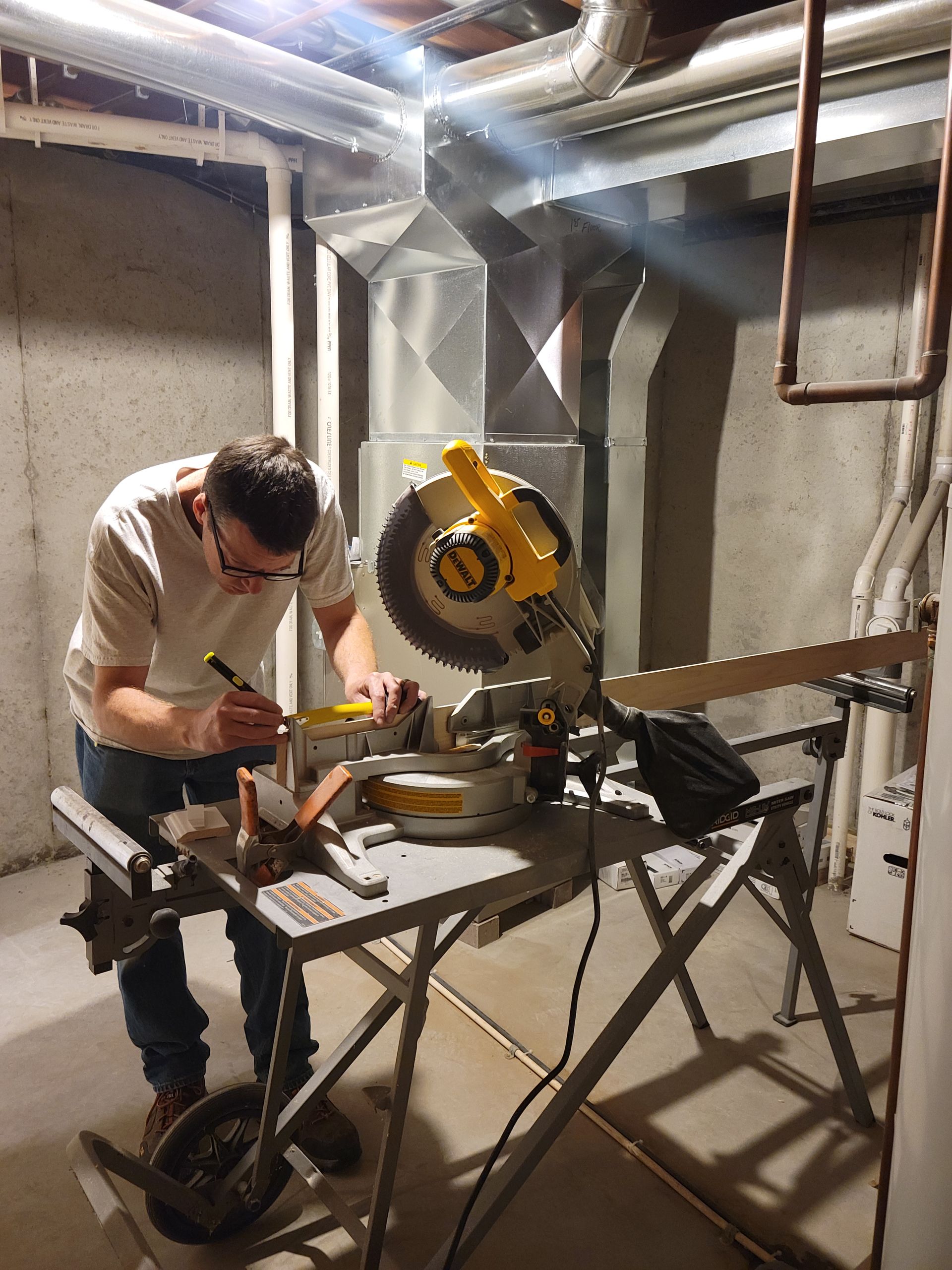 Person cutting metal with a yellow miter saw in an unfinished basement workshop.