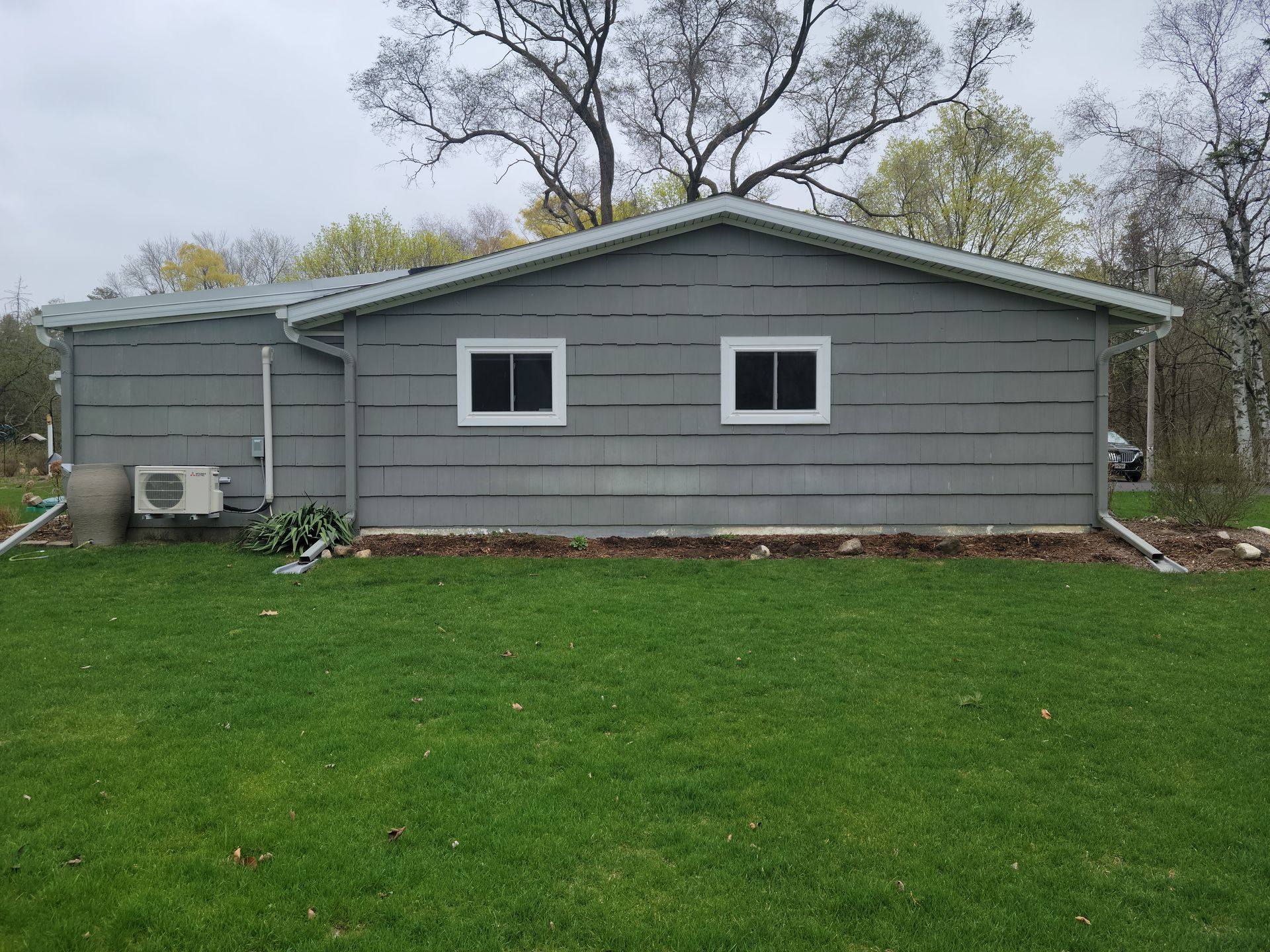 Gray house exterior with two windows and a green lawn in front