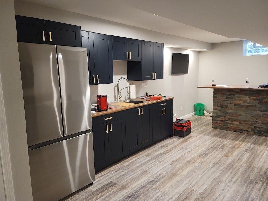 Basement kitchen with stainless steel fridge, dark cabinets, wood-look floor, and a small bar counter