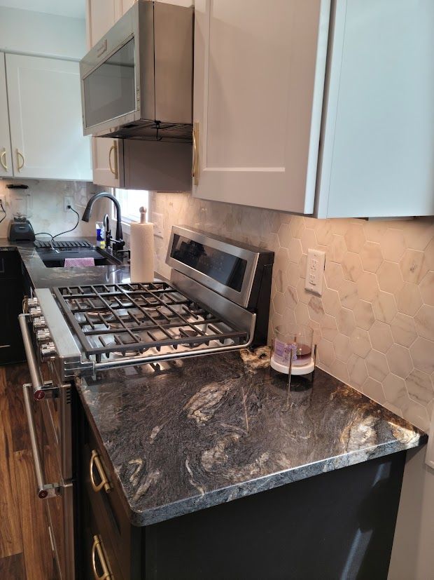 Modern kitchen counter with gas stove, stainless hood, dark countertop, and white cabinets