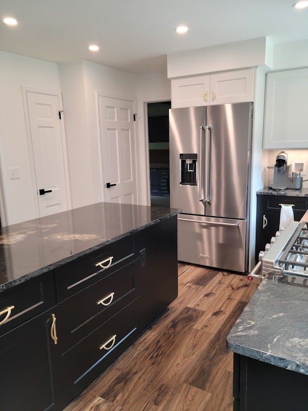 Modern kitchen with stainless steel refrigerator, black island, white cabinets, and wood flooring