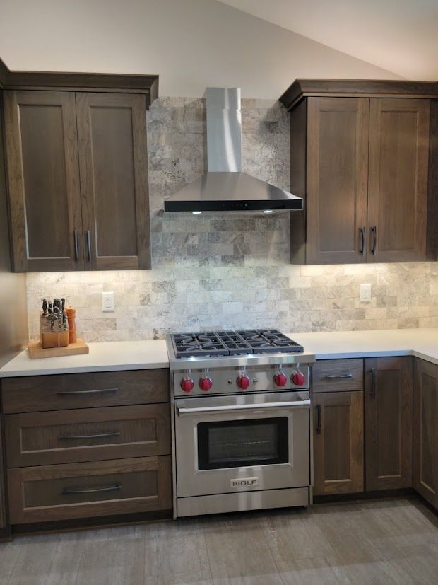 Modern kitchen with dark wood cabinets, stainless steel stove and range hood, and light countertops.