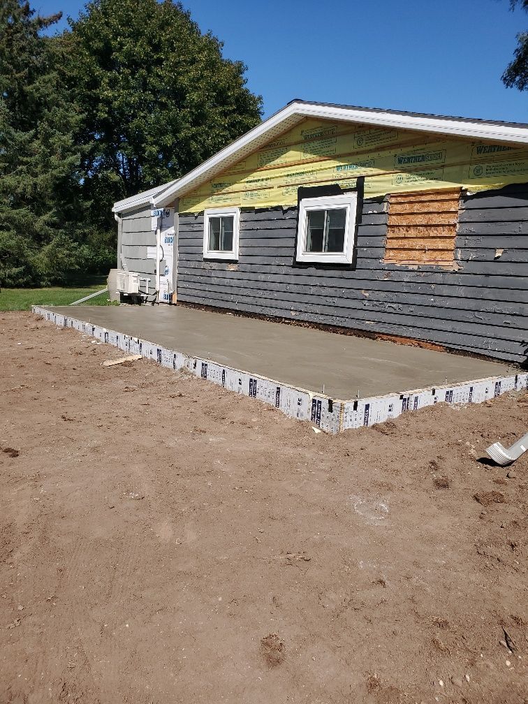 Single-story house with gray siding and a newly poured concrete porch in a dirt yard