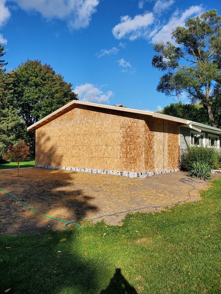 Small tan outbuilding with shingle siding in a sunny grassy yard under a blue sky