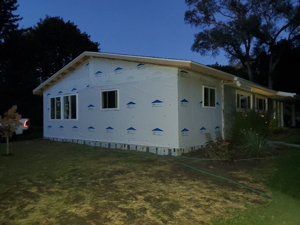 Partially sided house at dusk with white sheathing, blue wrap, and a grassy yard