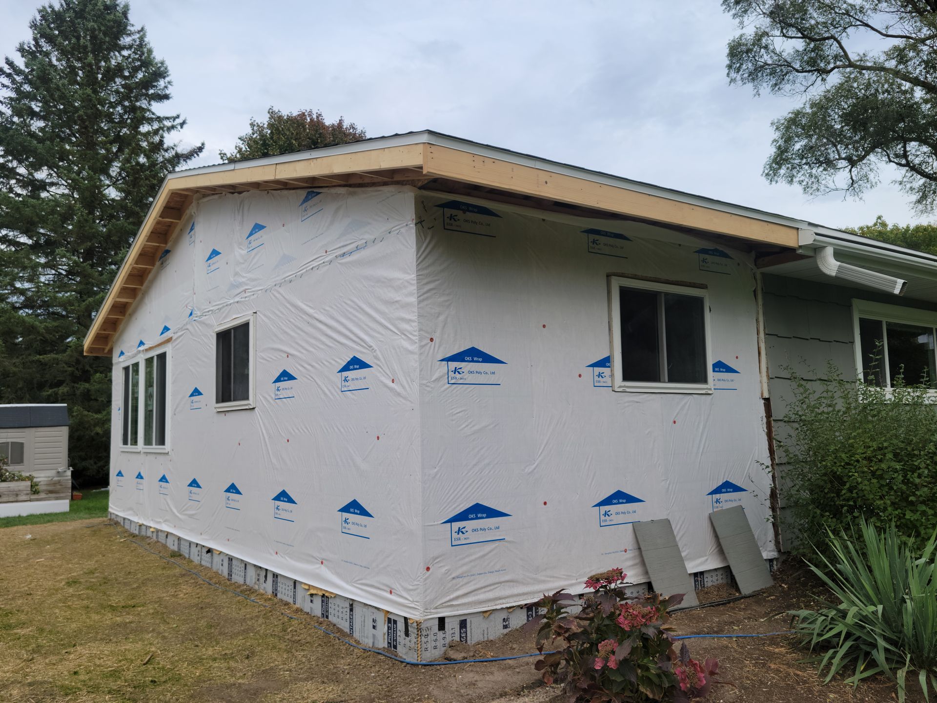 Partially wrapped house under construction with white siding and blue weatherproofing trim