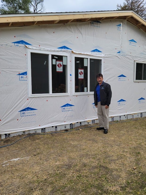 Person standing beside a white house wrapped in house wrap with a window and door under construction