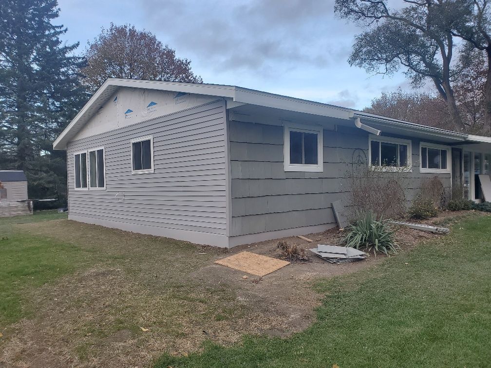 Single-story gray house exterior with white trim, windows, and a grassy yard under an overcast sky