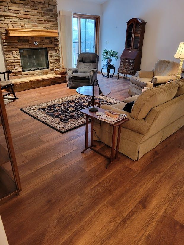 Cozy living room with stone fireplace, tan sofas, hardwood floors, and a window chair with lamp.