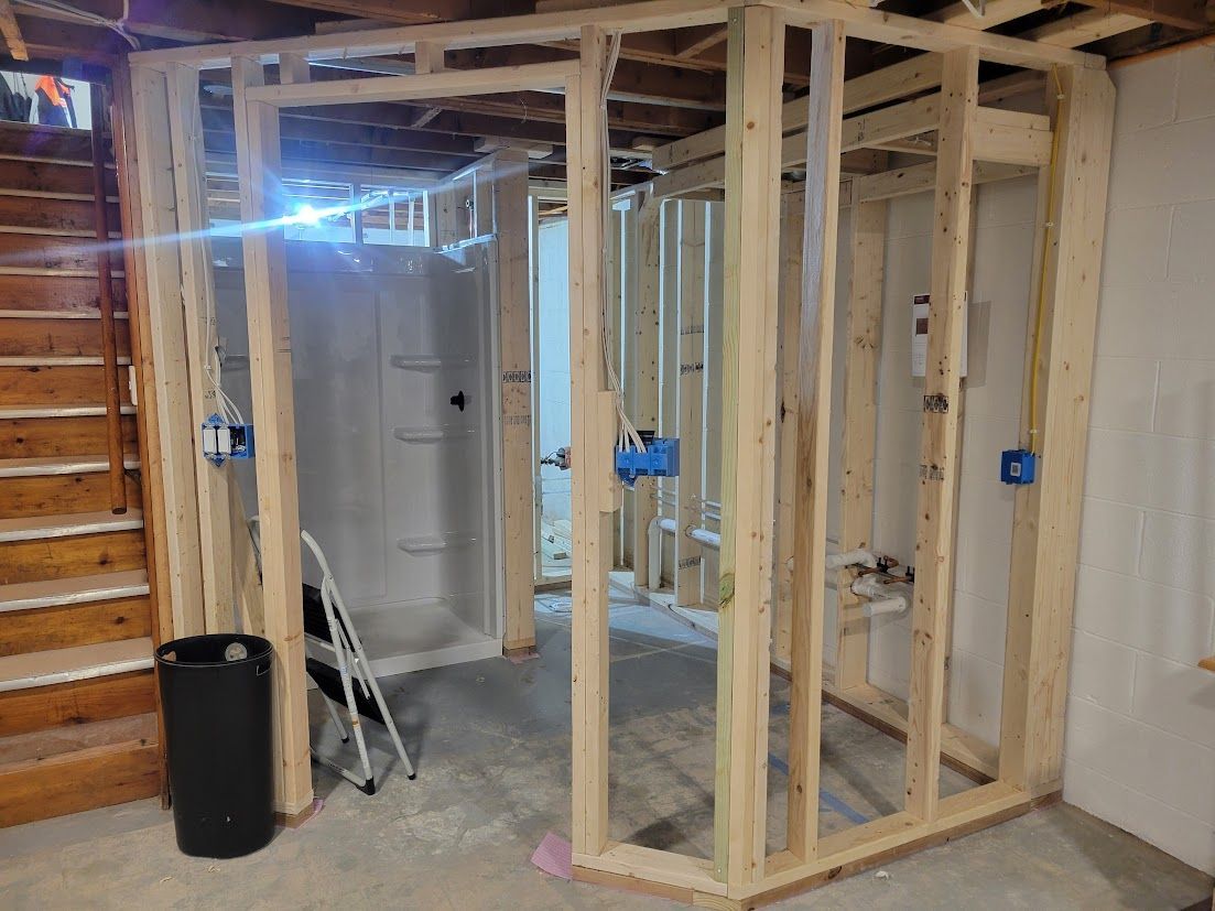 Basement under construction with exposed wooden framing, blue electrical boxes, and a ladder near a doorway
