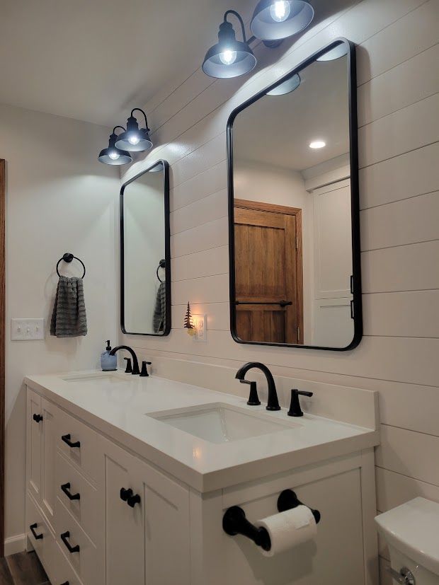 Bright bathroom vanity with two mirrors, black sconces, white sink, and towel rack