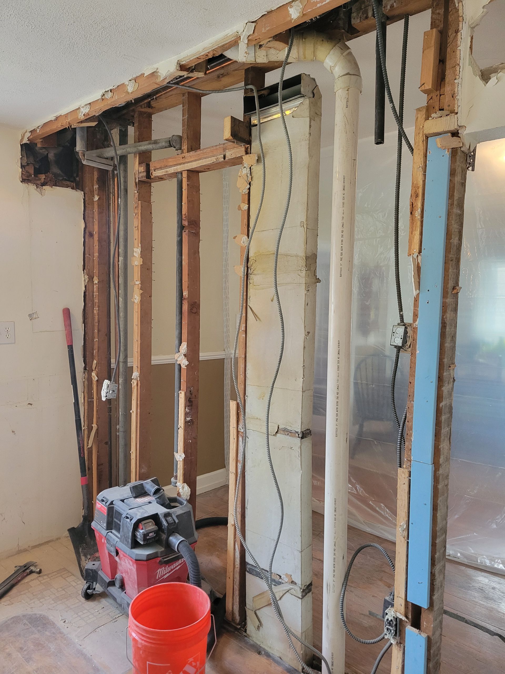 Interior wall under renovation with exposed studs, dangling wires, and construction tools on the floor