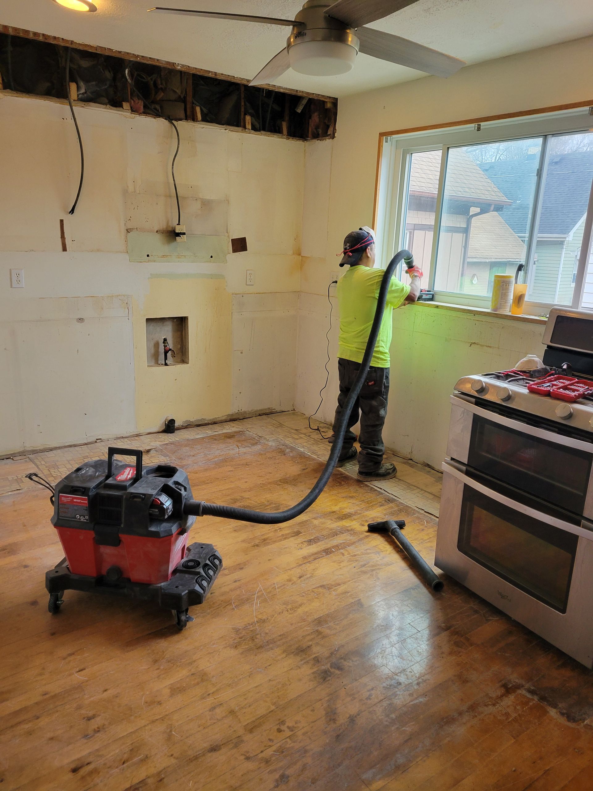 Person using a shop vac in a damaged kitchen with exposed wall and ceiling areas.
