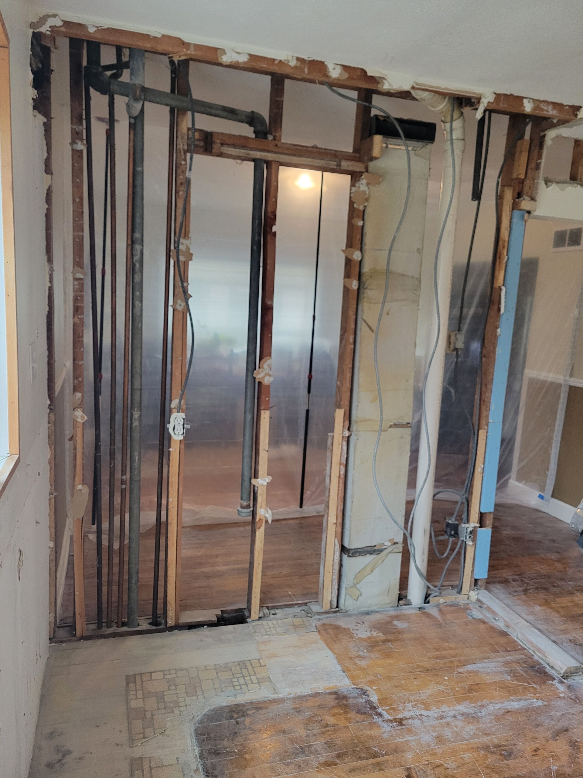Renovated interior wall with exposed studs, wiring, and open framing around a doorway.