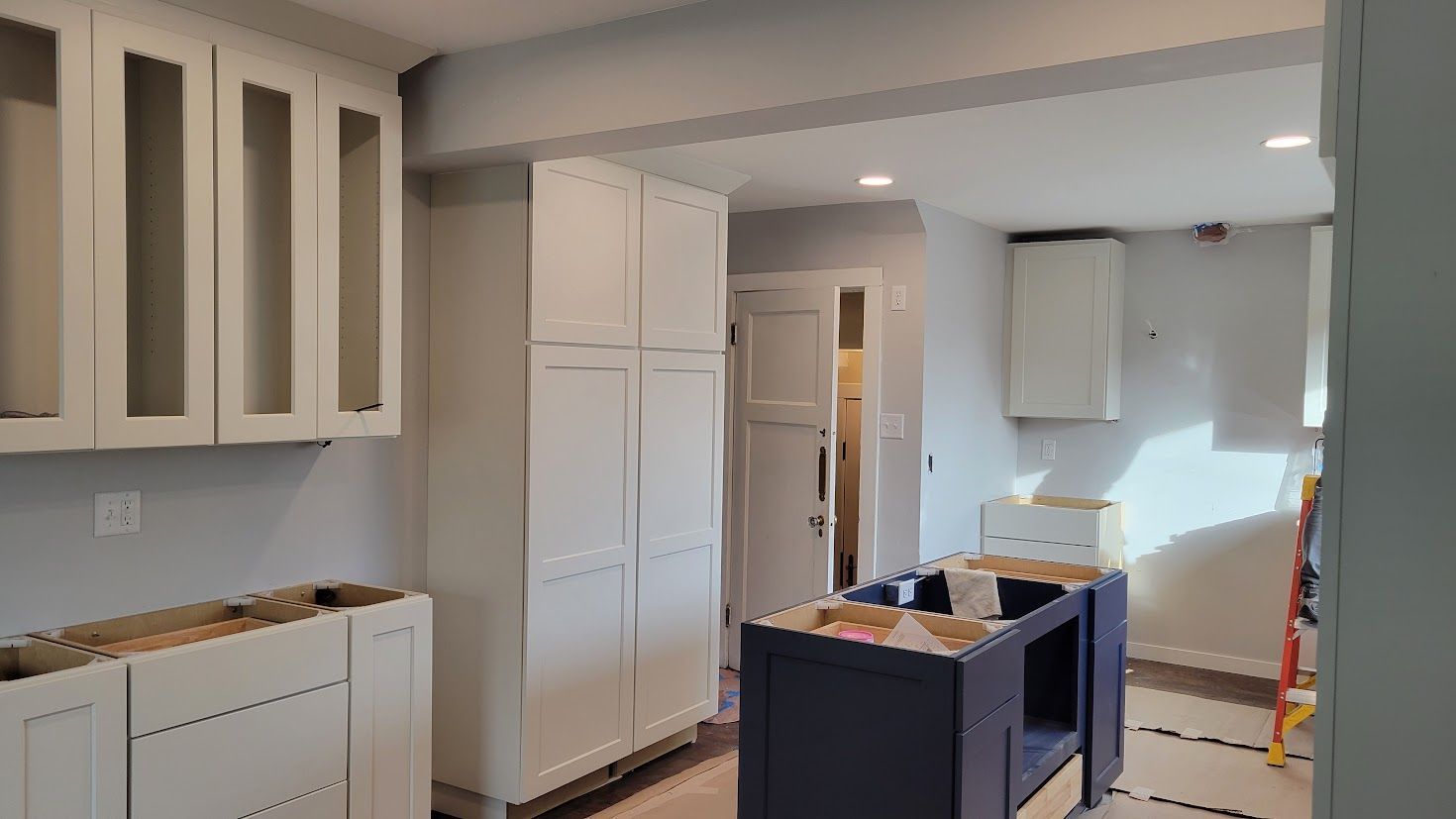 Kitchen under renovation with white cabinets, countertop, and a blue island cart in the center.