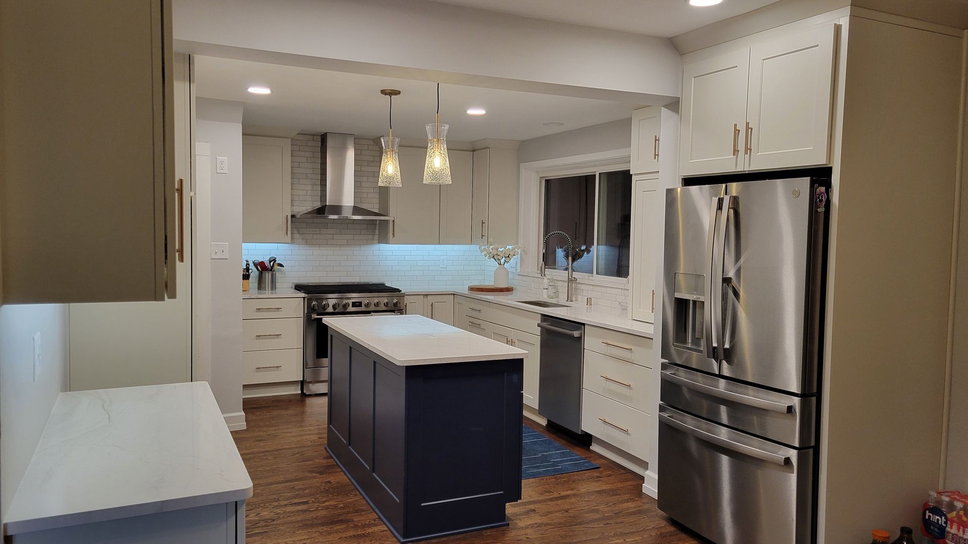 Modern white kitchen with island, pendant lights, and stainless steel refrigerator