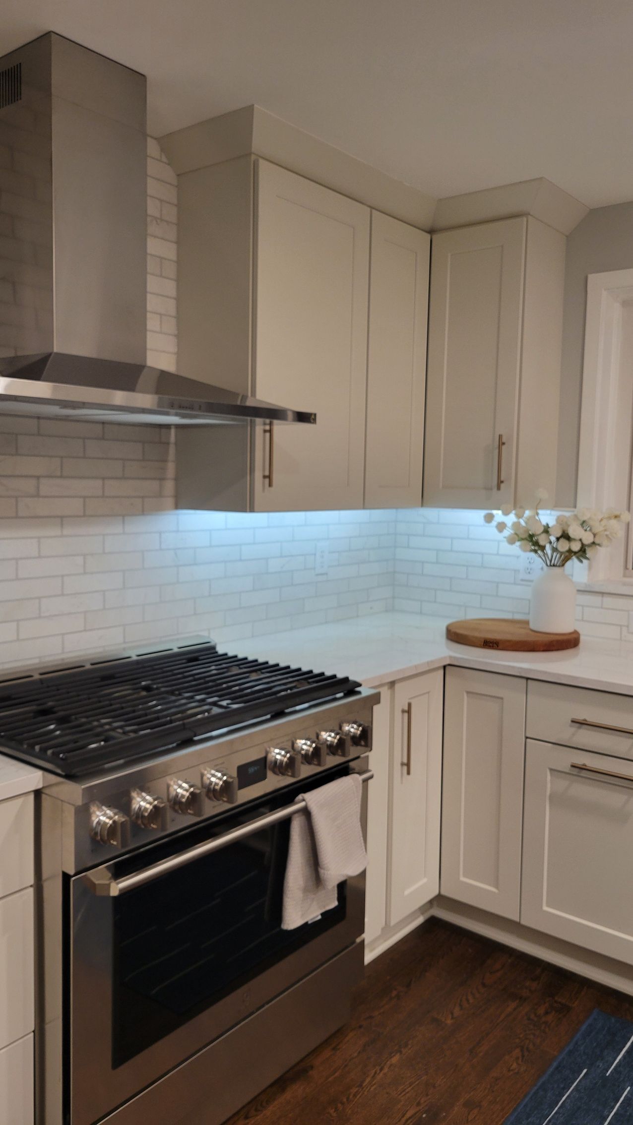 Modern kitchen with stainless steel stove, white cabinets, tile backsplash, and under-cabinet lighting