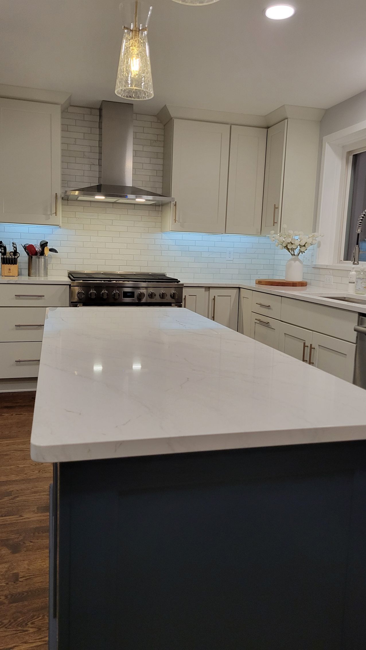 Modern kitchen with white island, marble backsplash, stainless range, and pendant light under cabinets.