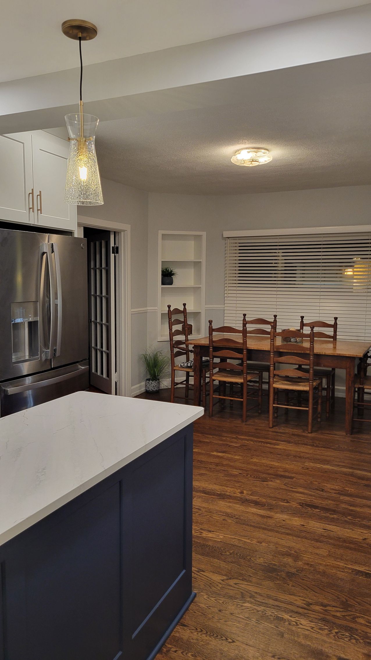 Modern kitchen and dining area with dark cabinets, stainless fridge, wooden table, and pendant light